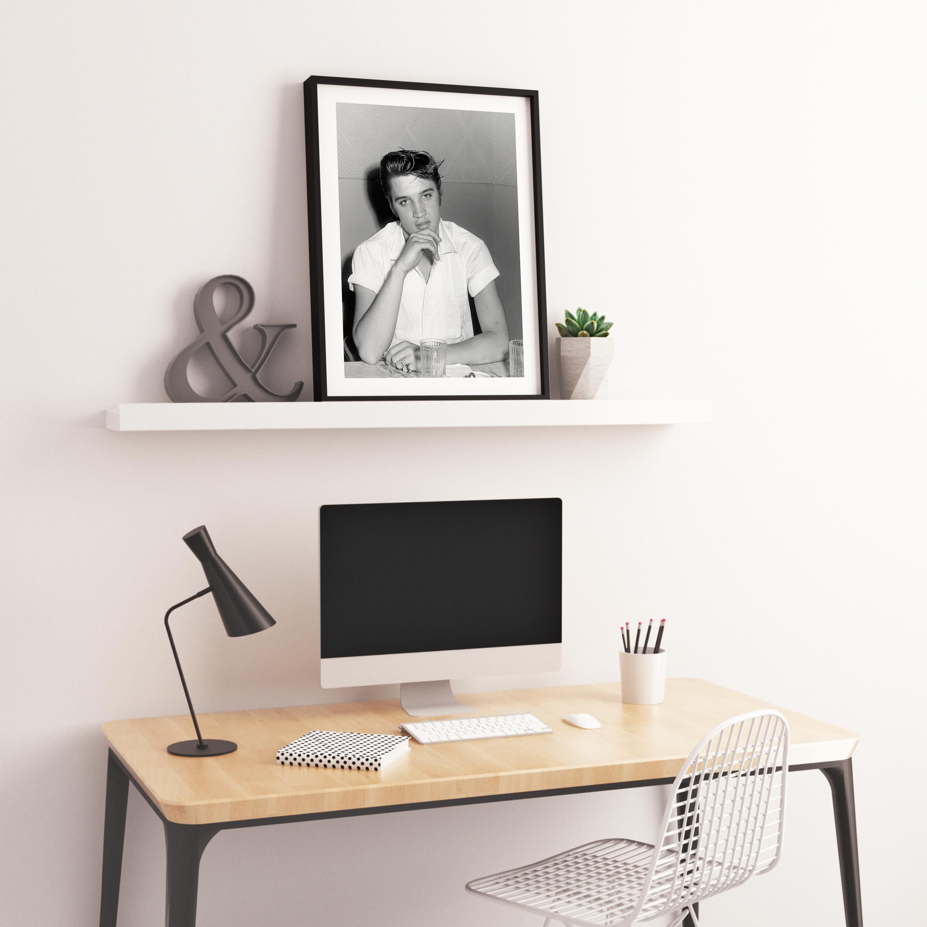 This awesome black and white portrait features Elvis Presley in his younger years, candid and seated at a table.

Elvis Presley was an American singer and actor. Regarded as one of the most significant cultural icons of the 20th century, he is often