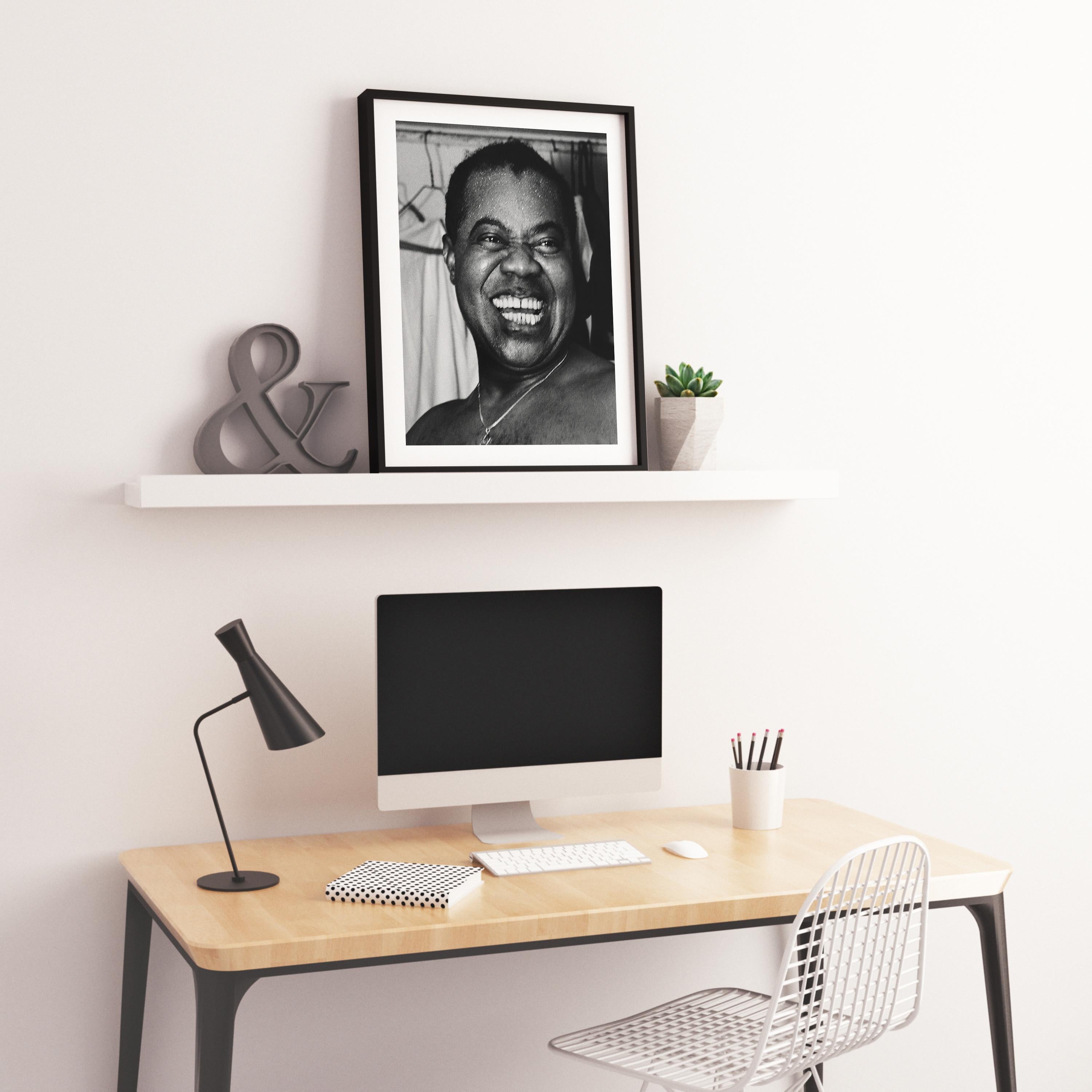 This black and white portrait features jazz legend Louis Armstrong laughing in a close-up candid shot.

Louis Armstrong was an American trumpeter, composer, singer and occasional actor who was one of the most influential figures in jazz. His career