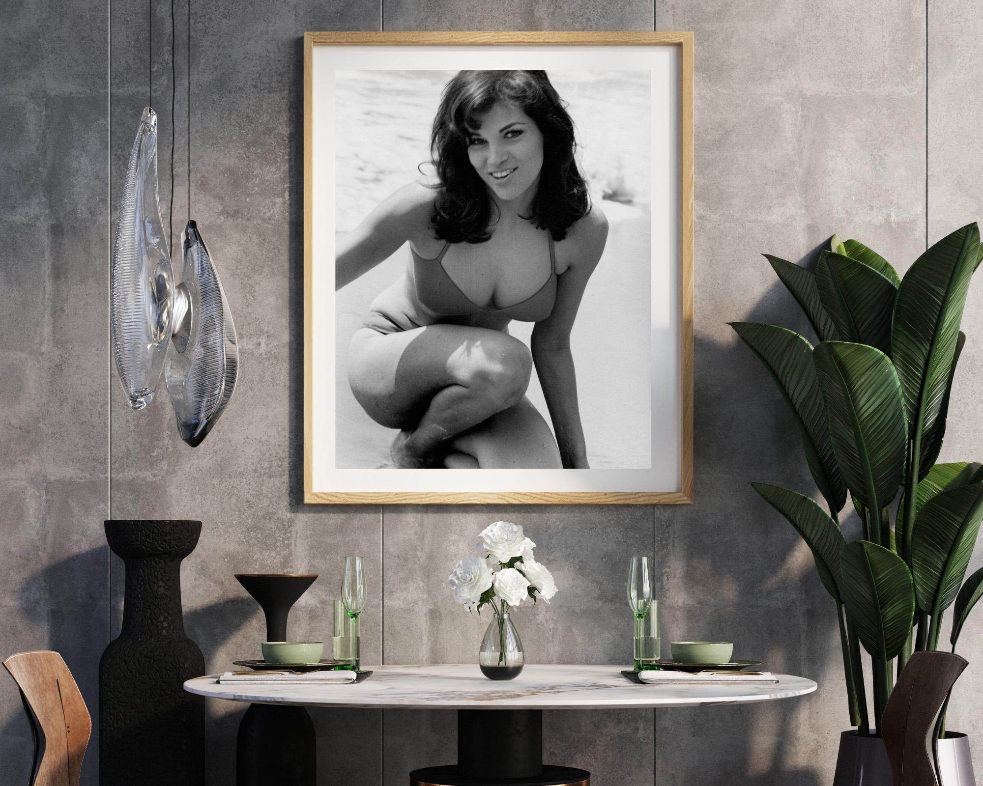 This black and white photo features Raquel Welch posing in a bikini on a beach.

Raquel Welch was an American actress and pop‑culture icon of the 1960s and 1970s, known for adventure films and for reshaping Hollywood’s image of the female