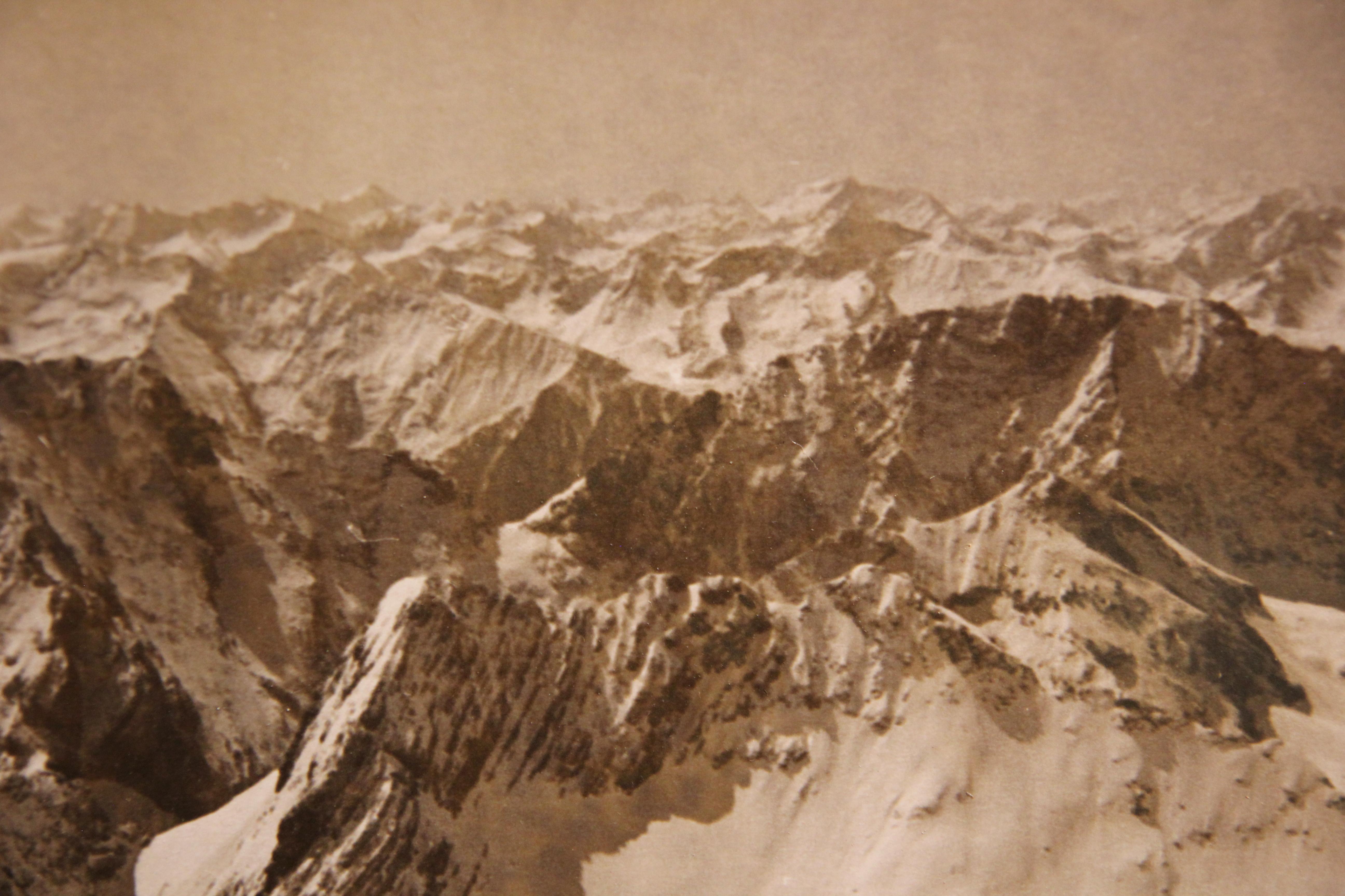 Photographie en noir et blanc de sommets de montagne enneigés. La photographie est attachée à une planche pour la protéger de la flexion.