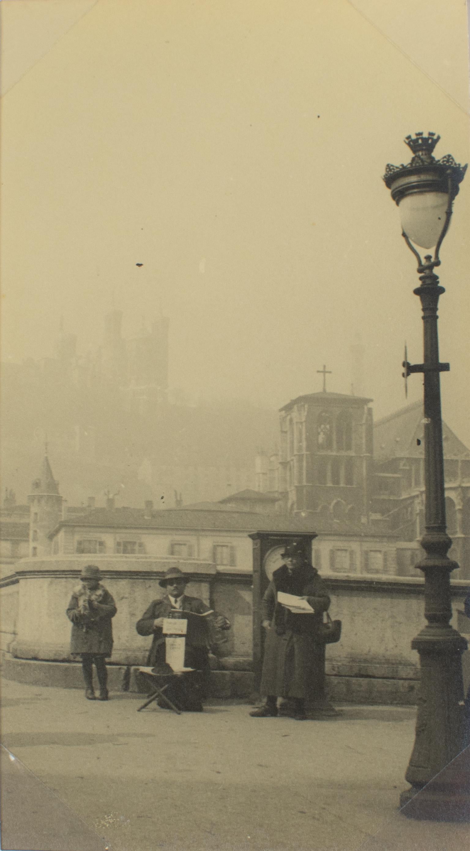 A unique original silver gelatin black and white photography. Street musician, and singer in Lyon, France, circa 1930. 
Street musician playing accordion with singers in Lyon, France, circa 1930. In the background in the fog, we can see The Basilica