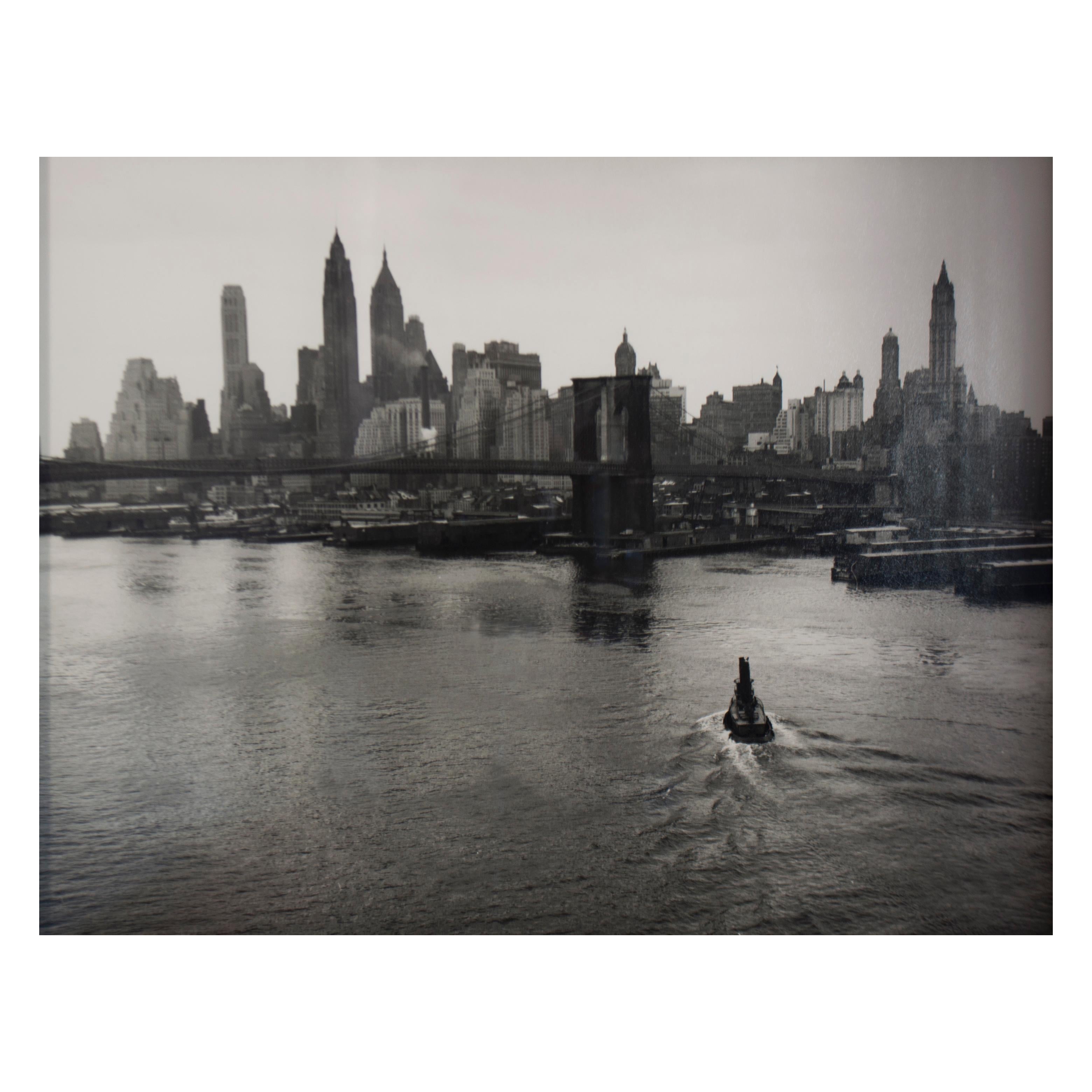 Cette photographie vintage en noir et blanc de Manhattan avec pont et rivière mesure 12.5" x 15.5". L'eau est au premier plan et couvre plus de la moitié de la composition à partir du bas de l'épreuve. Elle est généralement calme, avec de petites