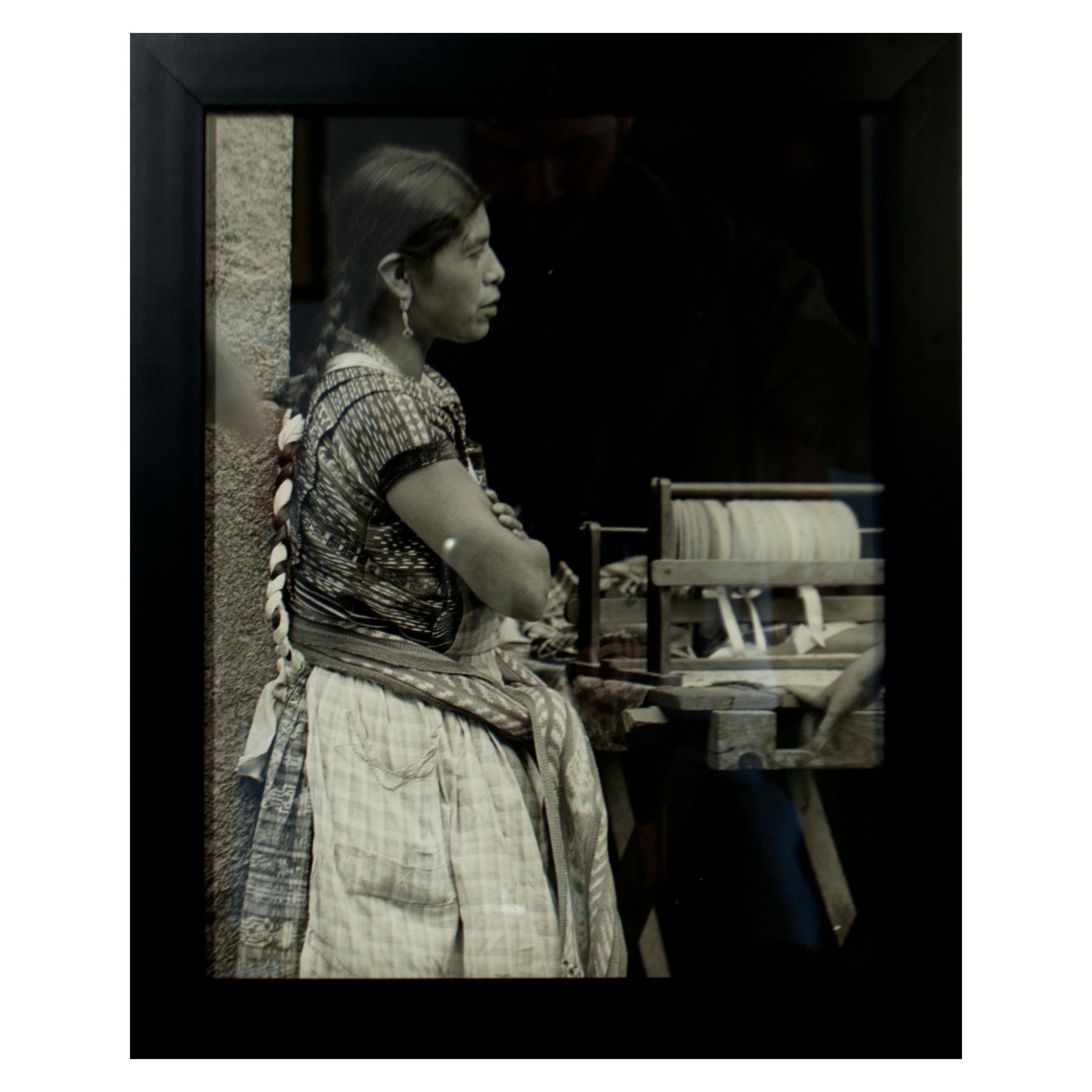 This 16"  x 13" black and white vintage photograph captures the side profile of an indigenous South American woman. The portrait is a 3/4 length portrait, depicting the figure from just above the knee and up, with her head positioned just slightly