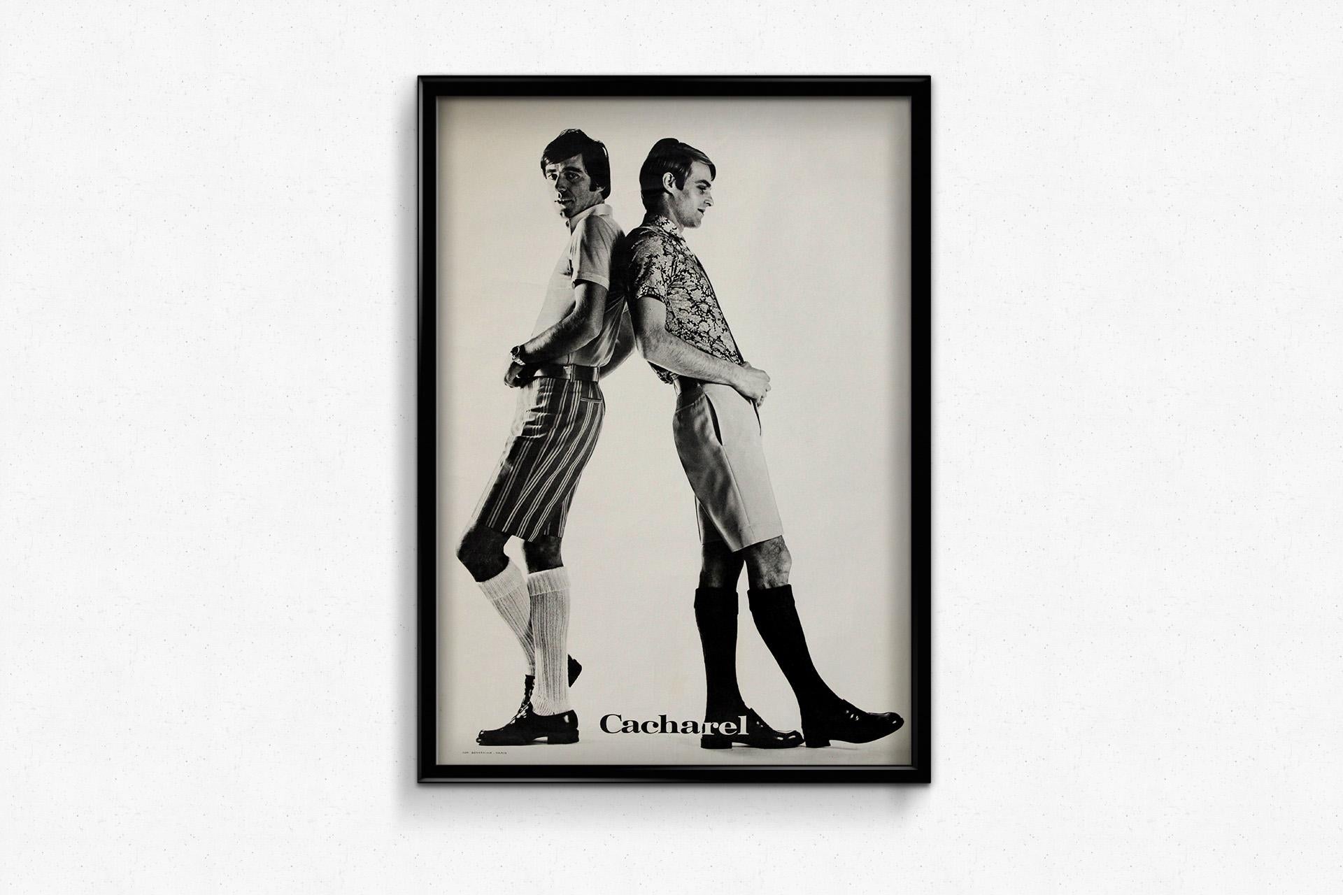 This circa 1960 original poster for Cacharel captures the essence of bold, youthful fashion that defined the era. Featuring two sharply dressed men in tailored shorts, patterned shirts, and knee-high socks, the image is a striking black-and-white