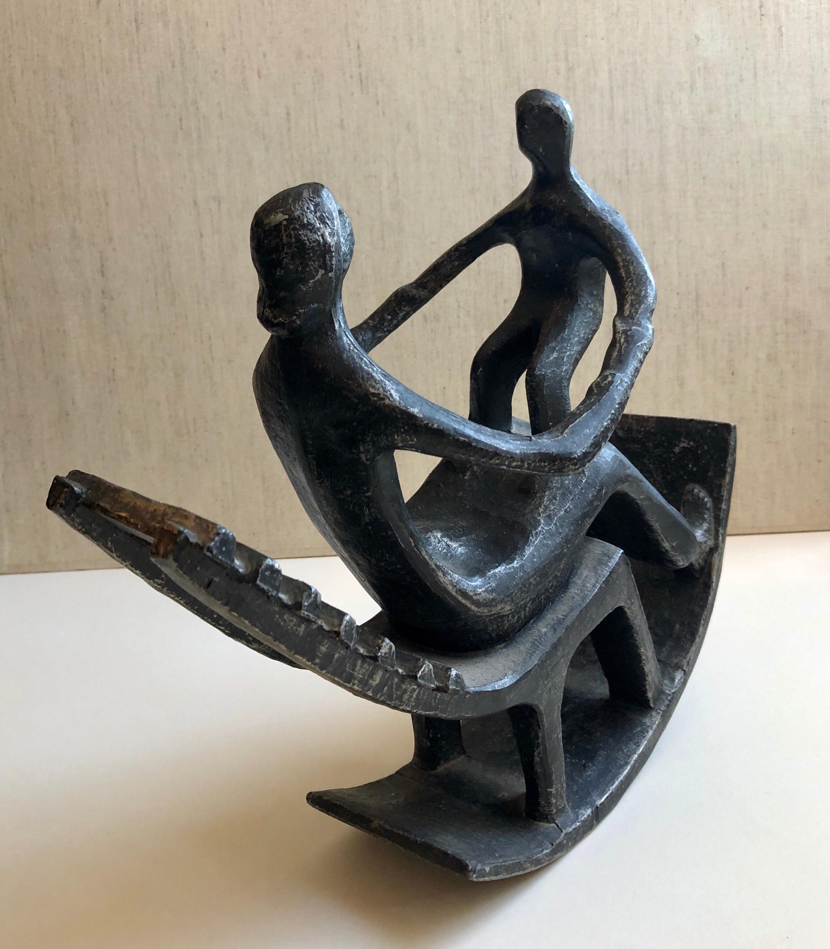 This is a cast metal sculpture of a woman and child, mother and baby in a rocking chair. It has a patina on a white metal. Not sure if it is steel or aluminum. It is and older vintage piece and has wear to patina where it sits and rocks on table. It