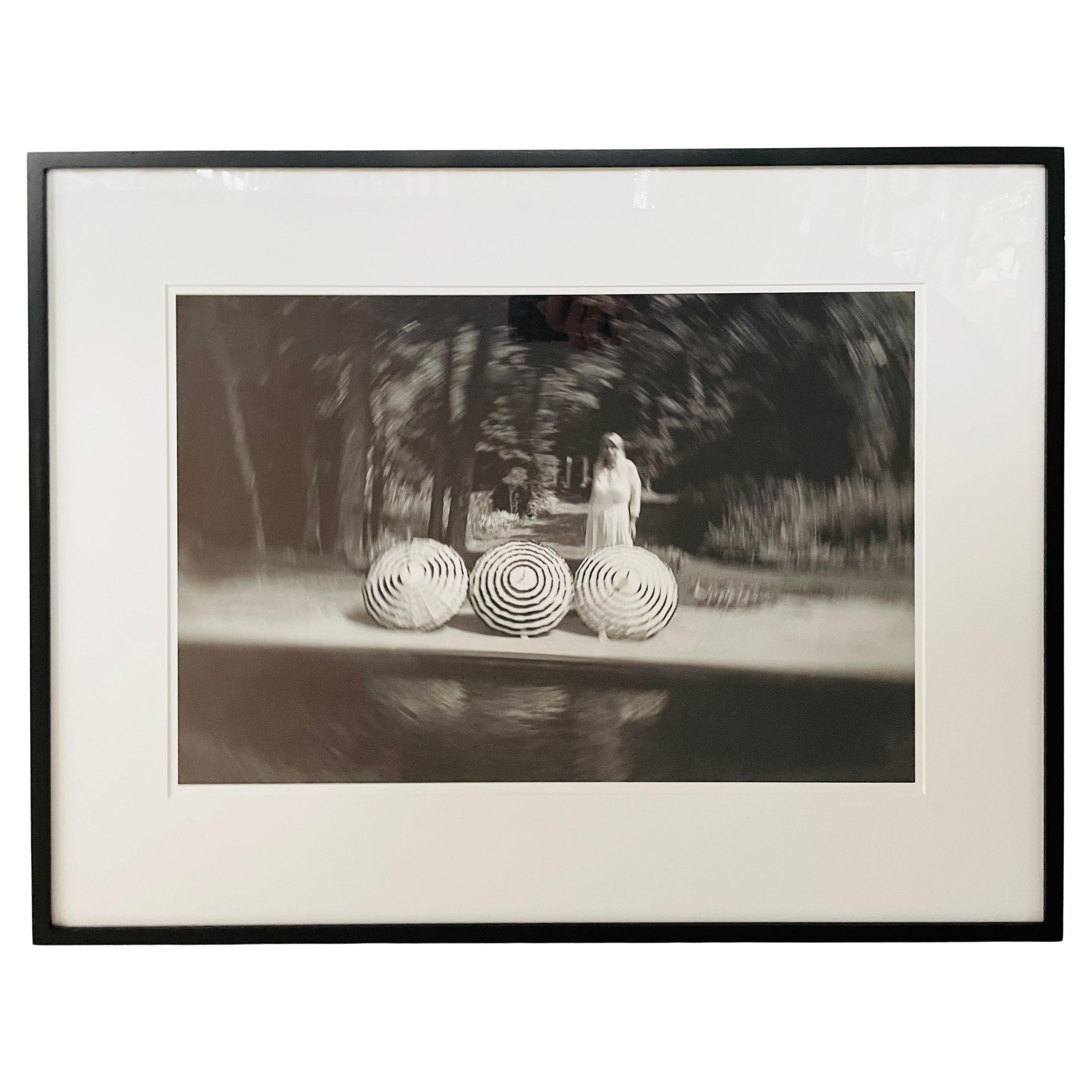 A modern genre photography archival pigment print titled " Bobbi's ghost" featuring a lady with three open umbrellas near a lake. The art work created by Luciana Pampalone ( American, 1963) is a limited edition numbered 1/20 and is part of the