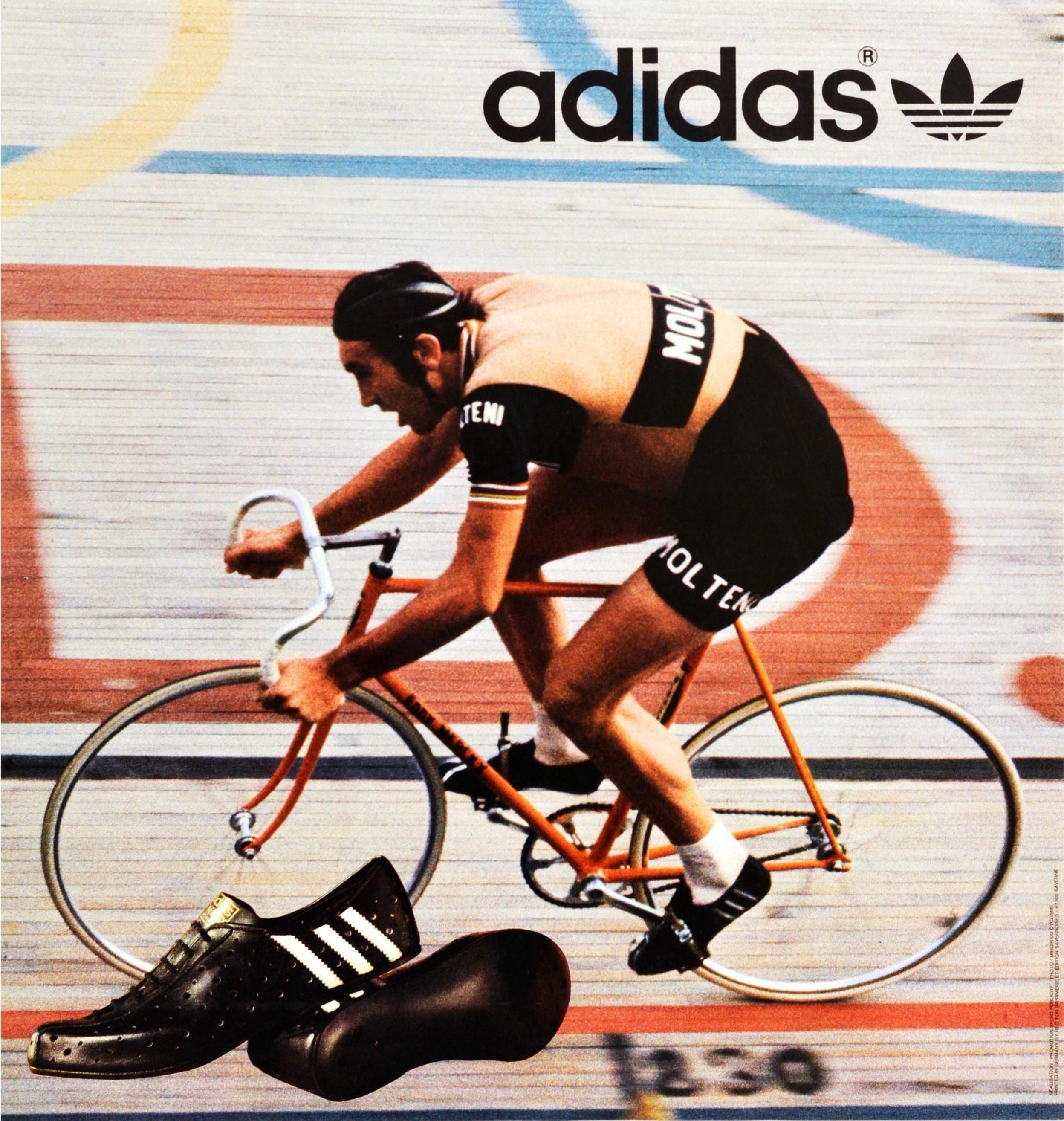 Original vintage advertising poster for Adidas shoes featuring a dynamic photograph of the professional road and track cyclist Eddy Merckx racing at speed in an indoor cycling event with the Olympic rings on the track in the background by the Adidas