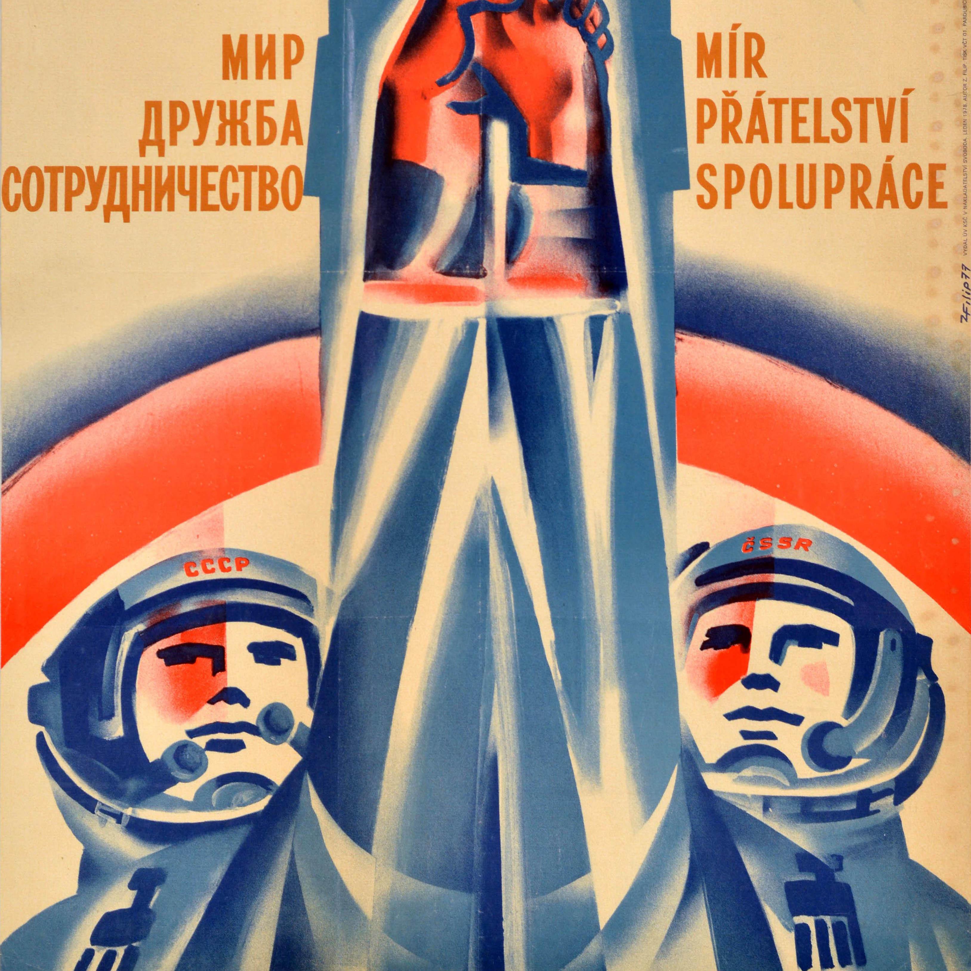 Original vintage Soviet propaganda poster featuring an illustration of two cosmonauts with USSR and Czech SSR on the helmets of their space suits, holding their hands up together against a rocket in the background with the caption in Russian and
