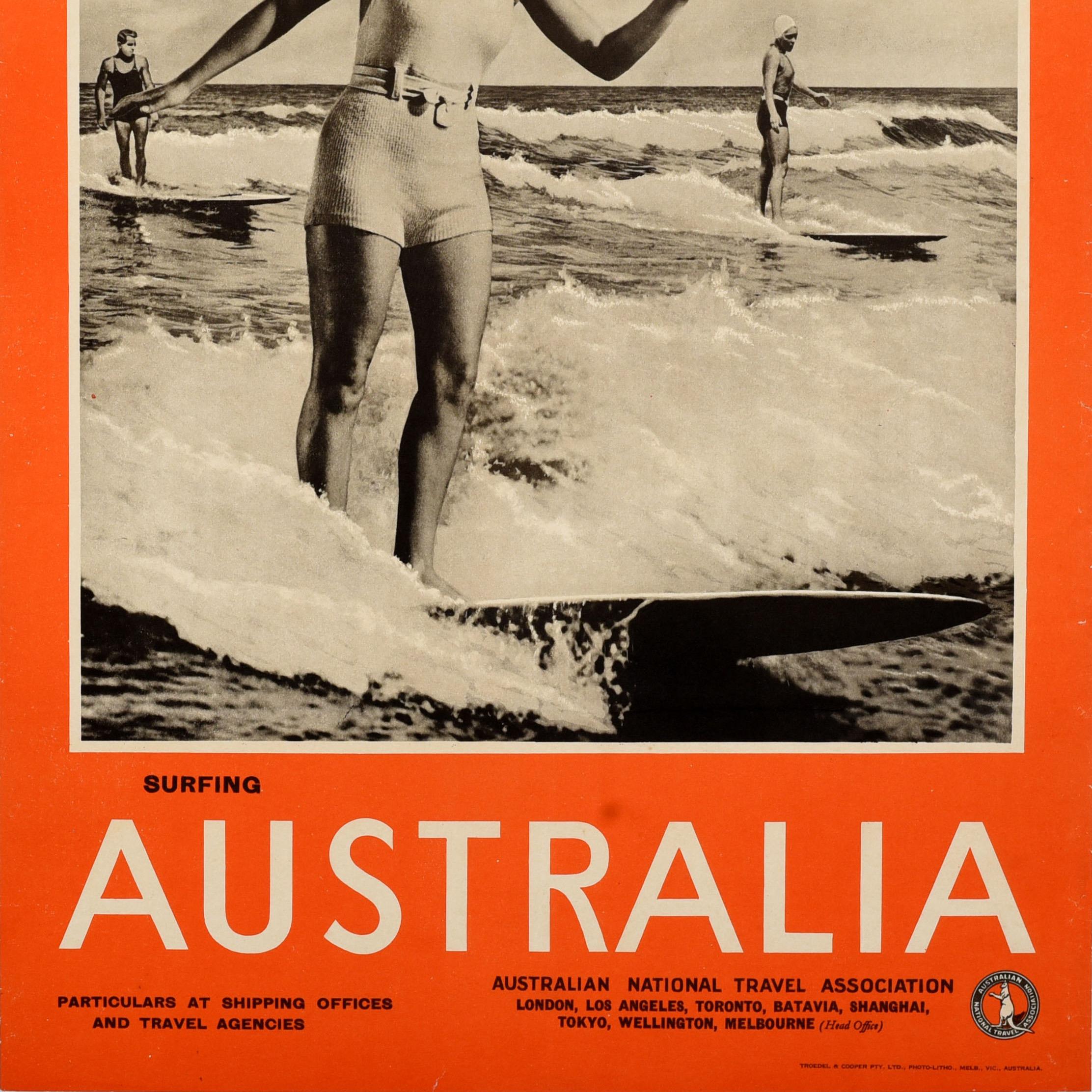 Original vintage sport themed travel poster - Surfing Australia - featuring a black and white photograph of a smiling lady in a swimming suit and cap surfing on a wave with two men on surfboards in the sea in the background, the image within a bold