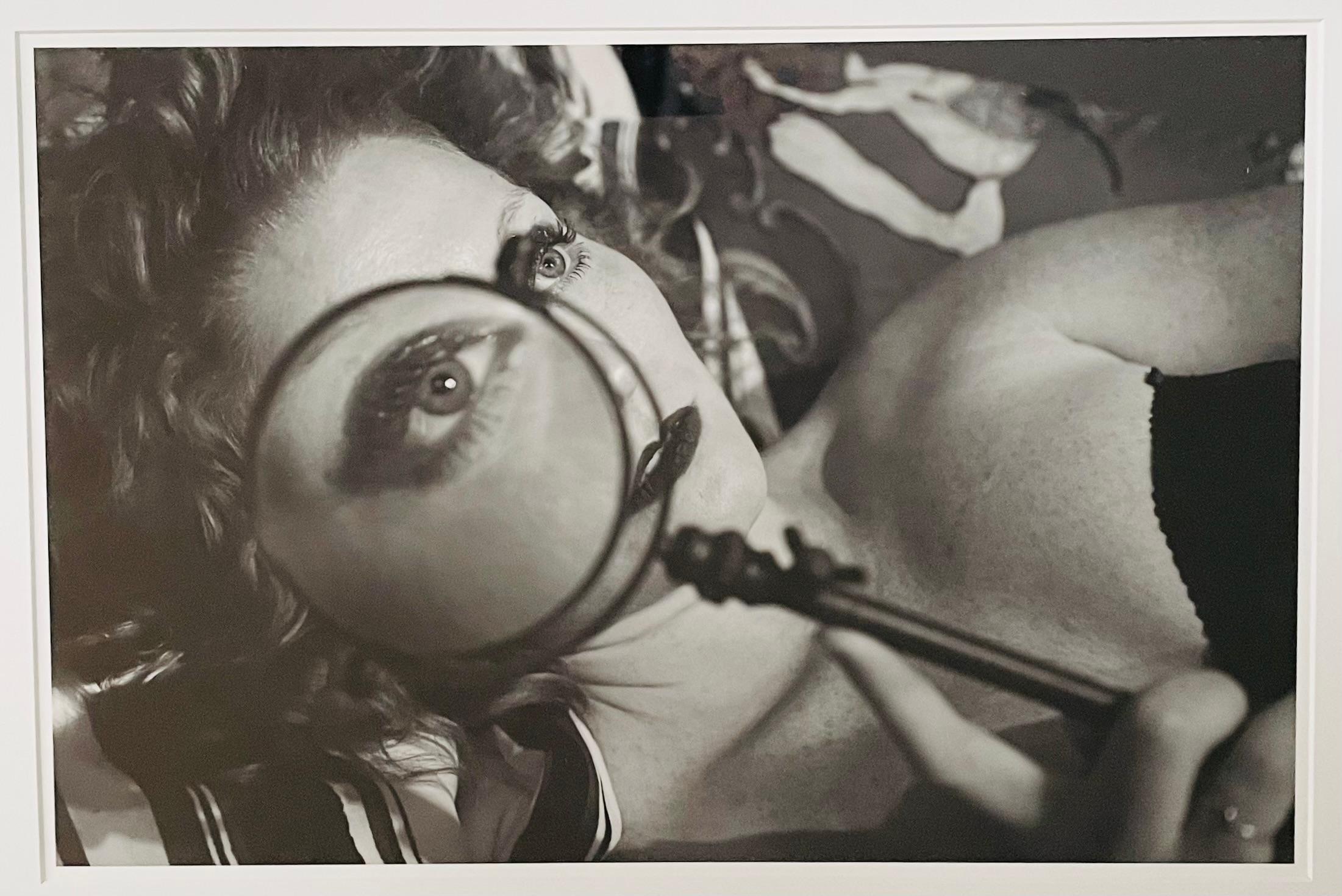 A photography archival pigment print of a a woman holding a reading magnifier close to her eye in black and white by Luciana Pampalone ( American, 1962) titled 