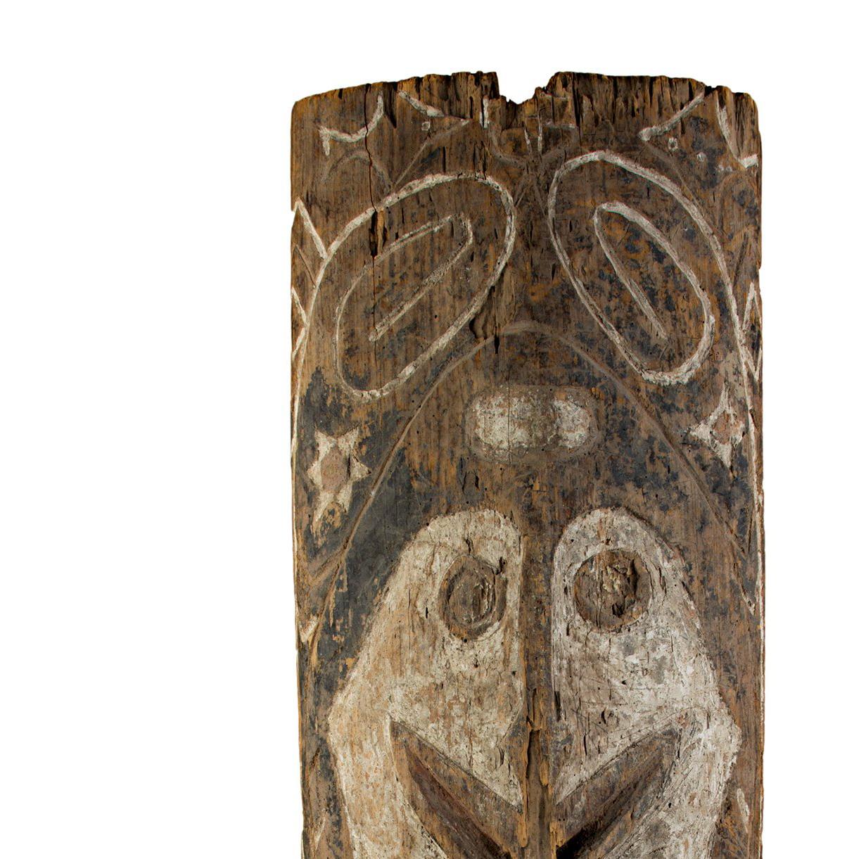 This half-shield from New Guinea is carved wood, embellished with vegetable pigment. It features an abstracted face with other designs. The shield is 31