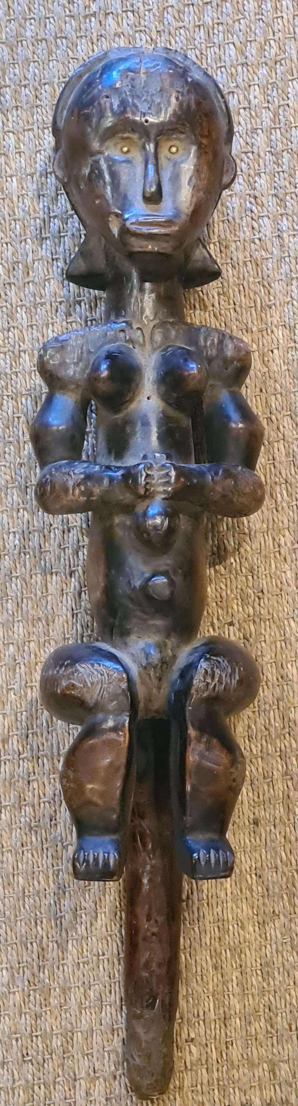 A Fine Fang Female reliquary figure, Eyema Byeri, seated with the hands held together on the abdomen, the muscular arms carved free of the body and holding a vessel to the abdomen, accentuated breasts, the short legs with thighs curving around to