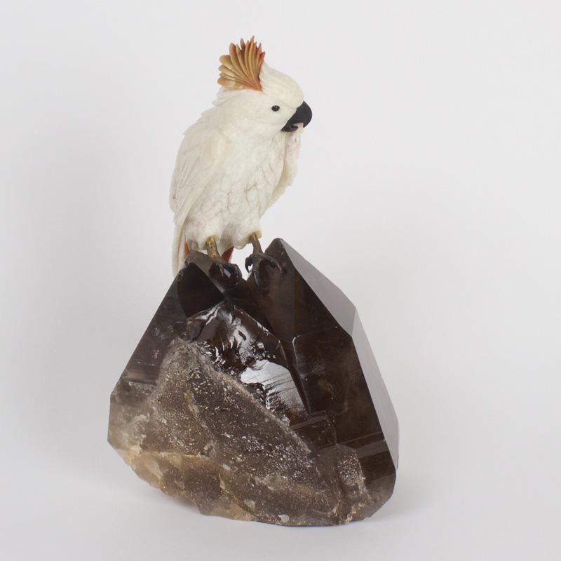 Amusing carved stone cockatoo with a quirky expression and brass feet mounted on an impressive smoky quartz specimen.
