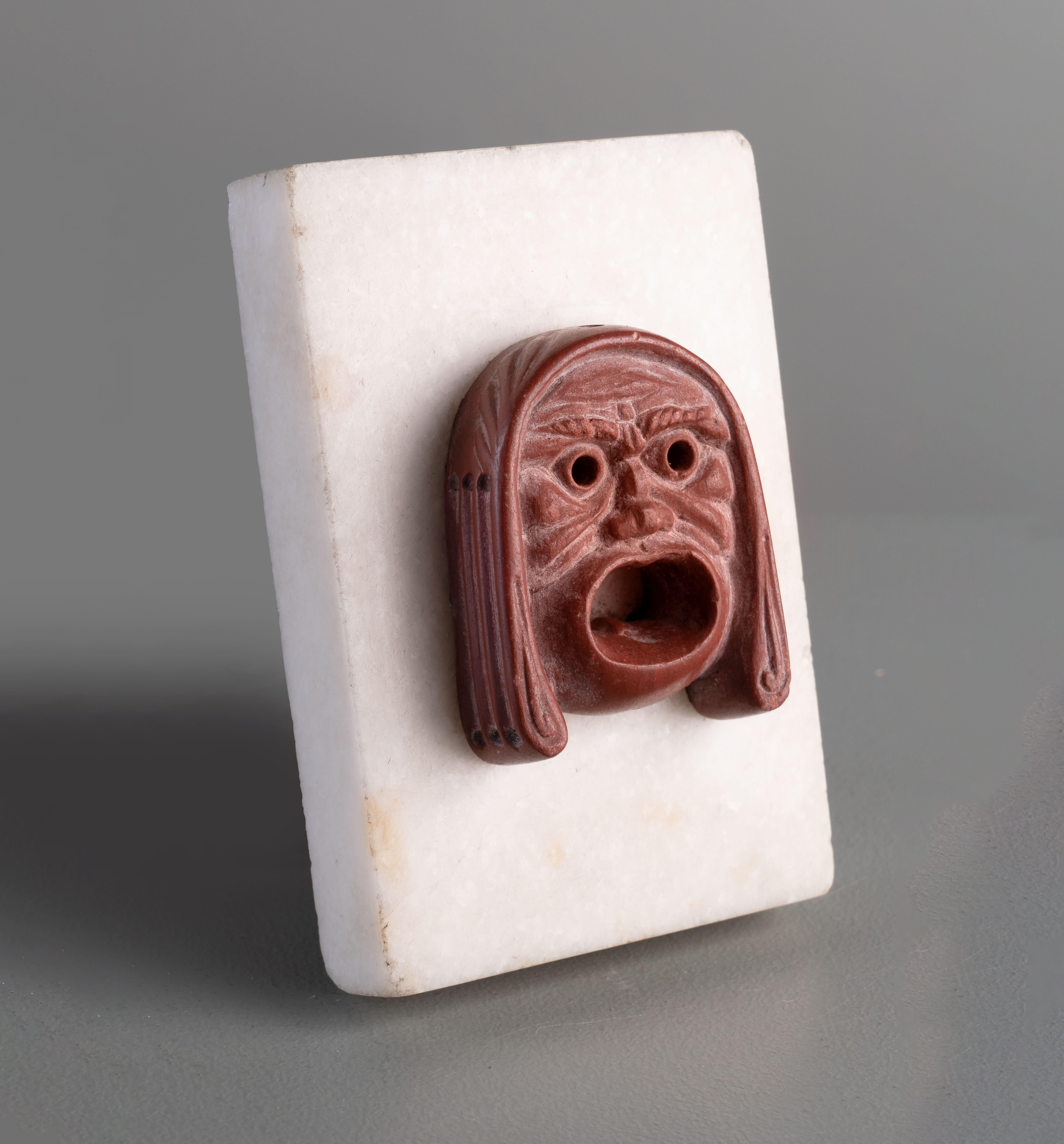 ROMAN RED JASPER APPLIQUE OF TRAGIC ACTOR
Rome, 1st Century A.D.
5.5 x 4.2 cm the mask
2 1/4 x 1 3/4 in

Provenance
Penicuik House, Midlothian, acquired by either Sir John Clerk, 2nd Baronet of Penicuik (1676-1755) or his son Sir James Clerk, of