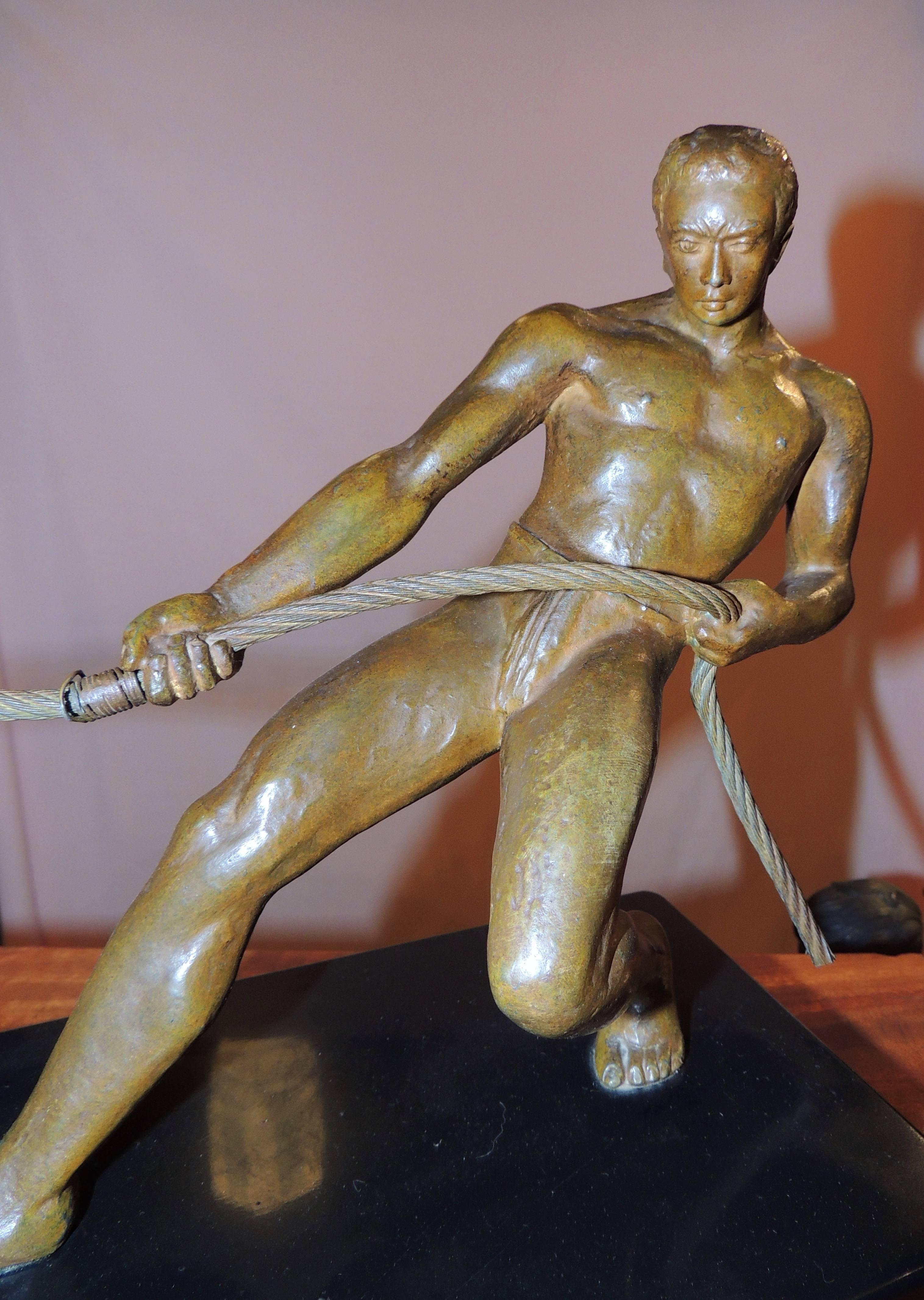 An Art Deco bronze sculpture of a man gripping a rope and pulling a rowboat ashore. It is a strong and unusual image, in contrast to the many images of men throwing spears or bending steel. This sculpture uses a section of the boat divided by a