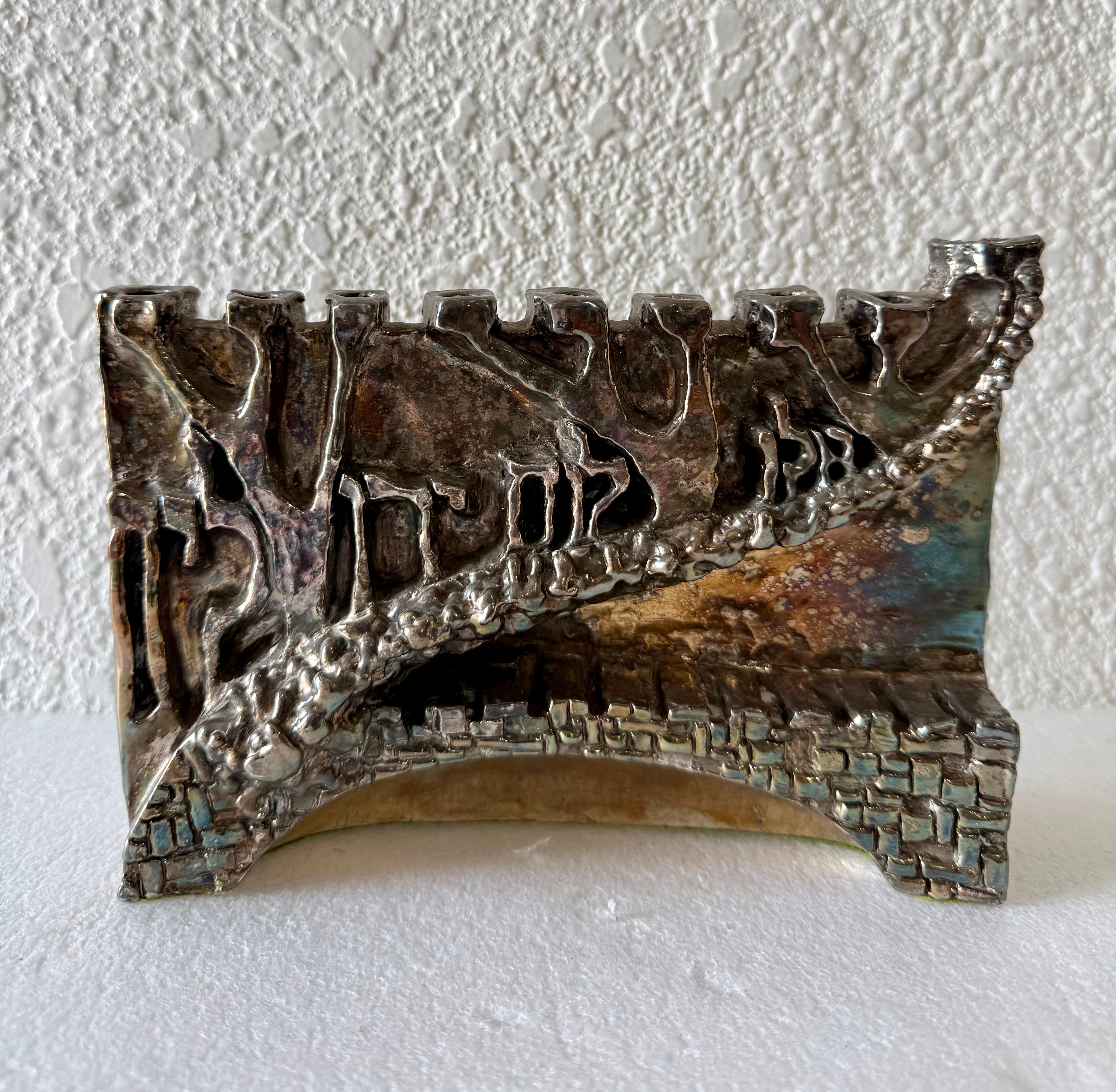 N. Levi (signed in Hebrew and English)
Menorah
Done in a brutalist design with the Hebrew words "Seek the peace of jerusalem"
Dimensions: 8 X 9 X 2.5 inches
This appears to be silver plated as I do not see a silver standard mark or hallmark.

There