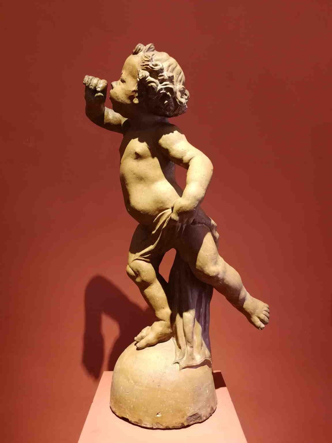 Questa statua in terracotta in eccellente stato conservativo considerata l'età e la fragilità del materiale,  raffigura un putto nell'atto di soffiare, colto in una posa di intenso plasticismo. L'opera è totalmente cava all'interno, segno di una sua
