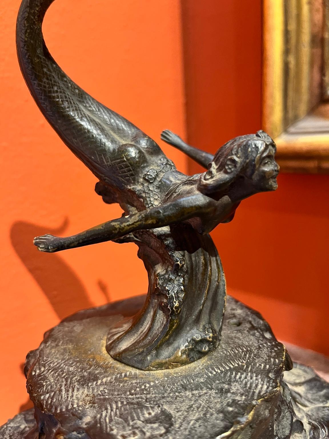 Bronzetto decorativo in stile Art Nouveau dei primi del Novecento raffigurante una sirena sorridente portata da un'onda sopra una fontana con un mascherone. 
Il riferimento è alla fiaba dello scrittore Hans Christian Andersen come si vede dalla