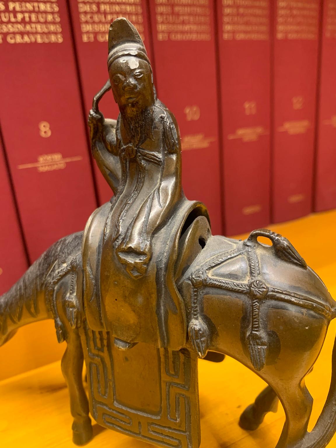 Estatuilla oriental china de bronce de 16,5 x 16 cm que representa a un sabio montado a caballo. Obsérvese la precisión de los detalles, desde las borlas de los arreos hasta la montura inferior con decoraciones geométricas en forma de laberinto,