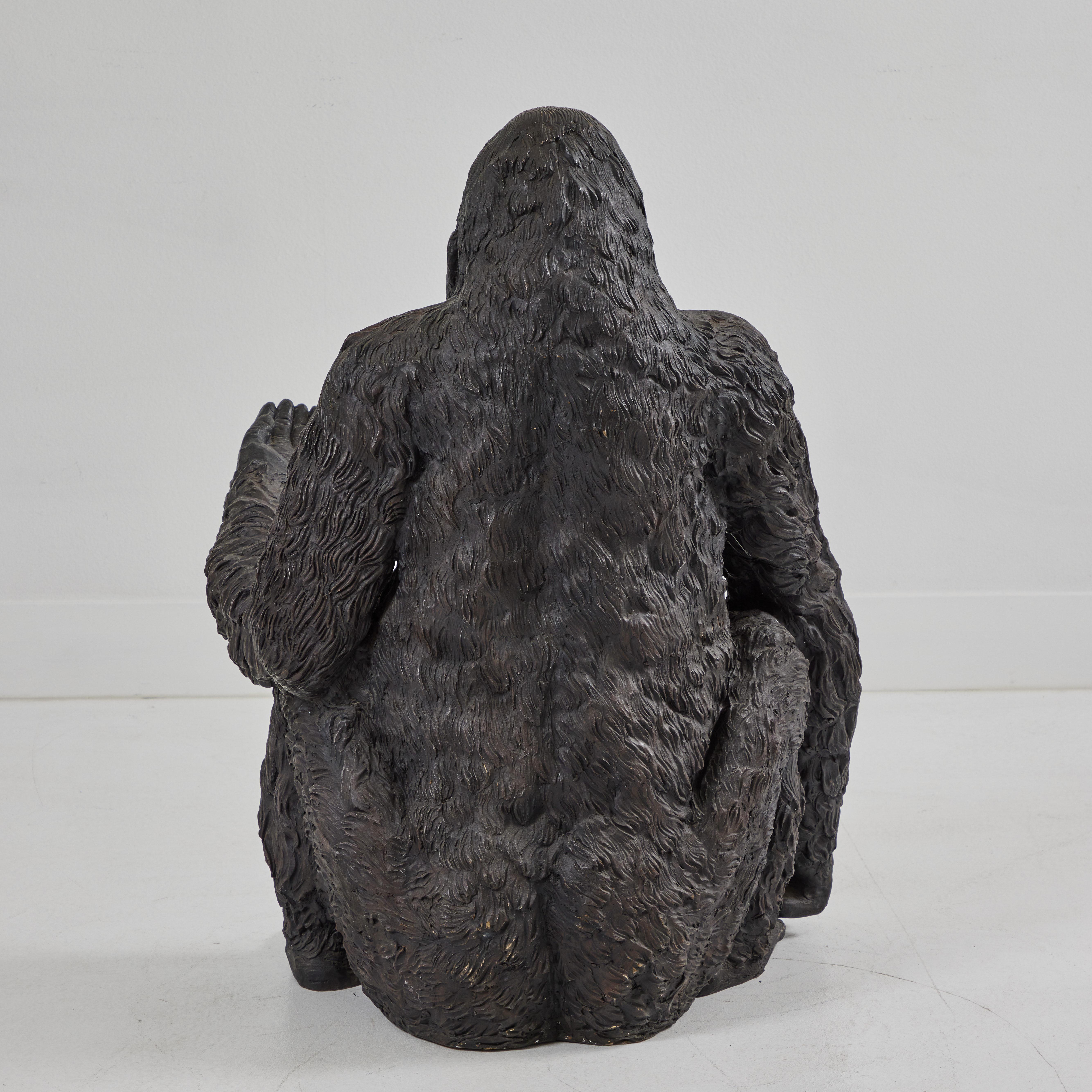 Ce gorille en bronze est assis astucieusement, la main gauche tendue et le bras droit détendu vers le sol. Les yeux de verre sont noirs et reflètent la lumière environnante, ce qui donne à cet animal un visage plein de compassion et de vie. La