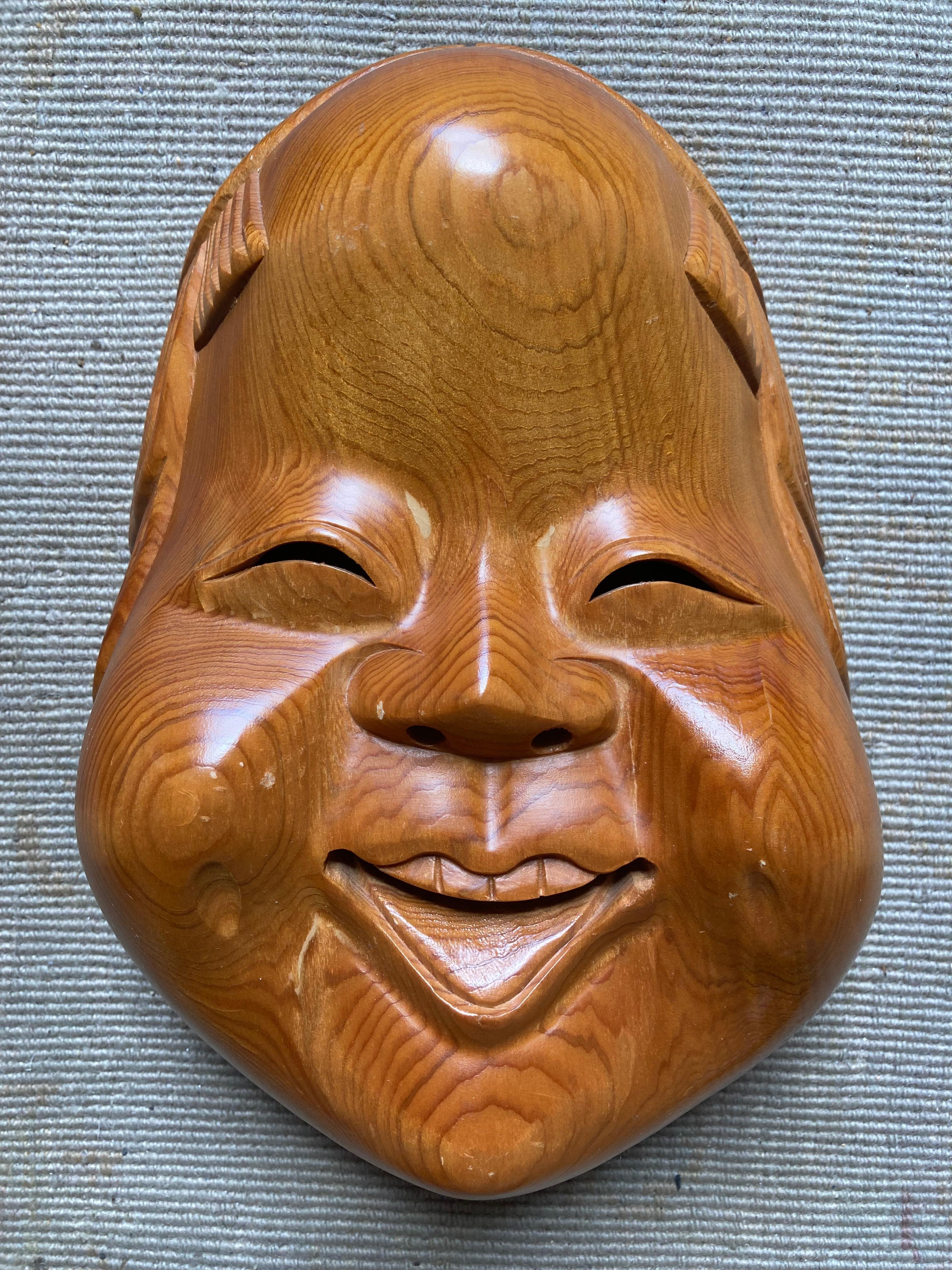 Une collection de cinq masques de théâtre nô japonais fabriqués à la main, dont quatre en bois sculpté et un (le plus grand, celui qui est noir et rouge sur une moitié et blanc sur l'autre) en papier mâché. La plus grande mesure 15