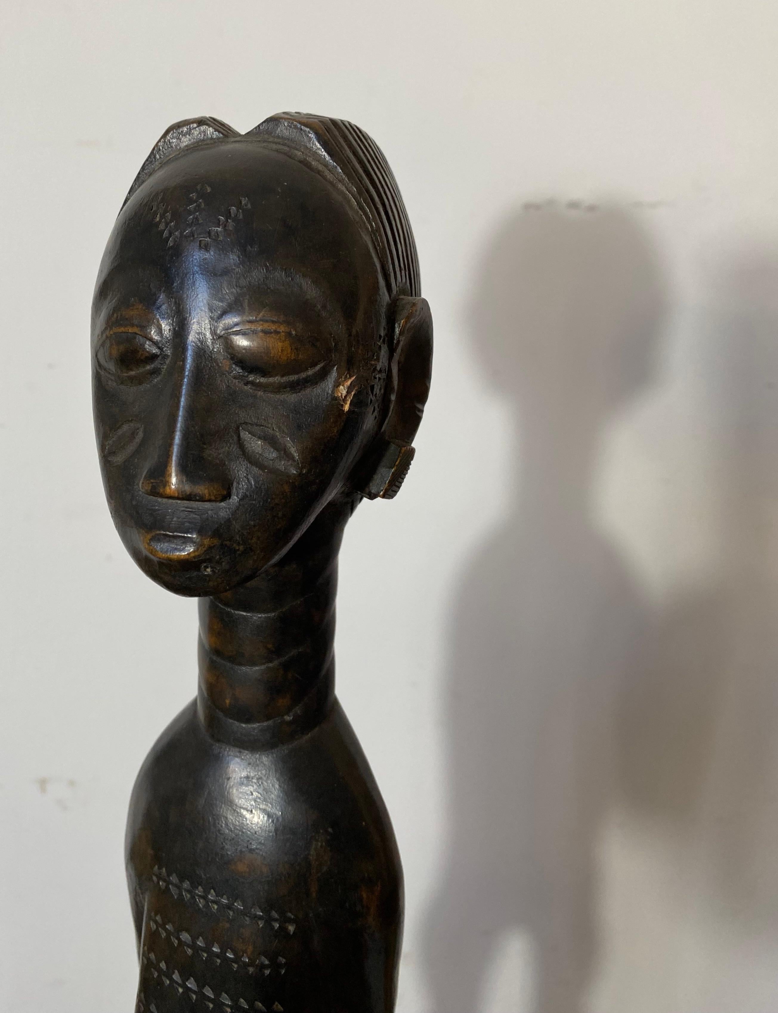 An elegant African sculpture from the West African Baoulé or Baule people, depicting a young woman wearing a loincloth. Smooth black lightly worn patina.