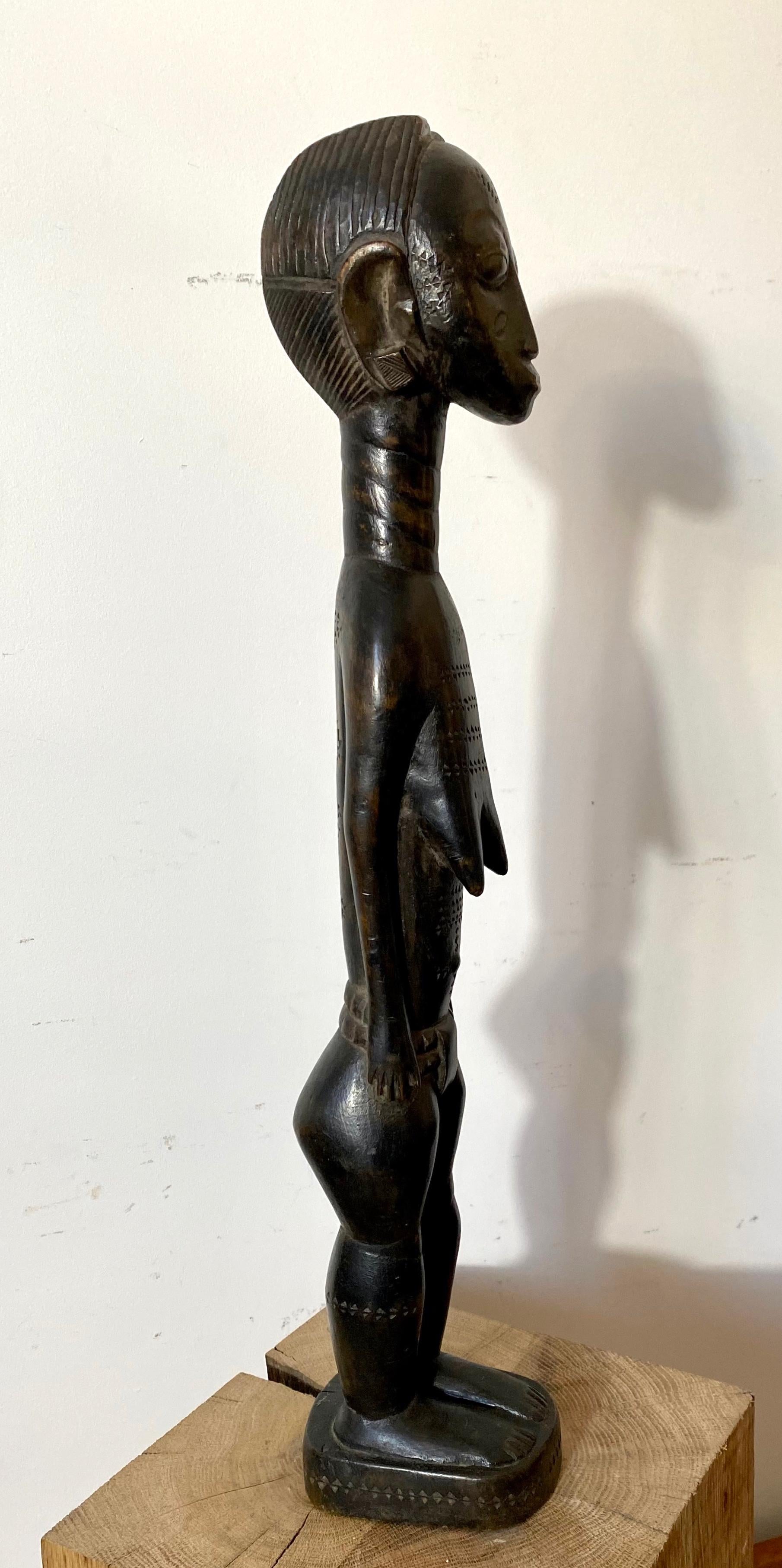 Eine elegante afrikanische Skulptur aus dem westafrikanischen Volk der Baoulé oder Baule, die eine junge Frau im Lendenschurz darstellt. Glatte schwarze, leicht abgenutzte Patina.