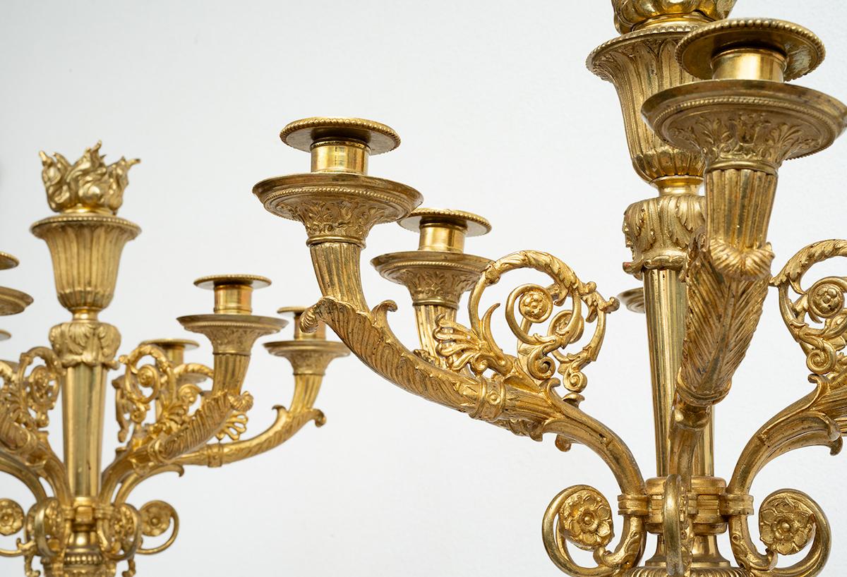 Pair of French Napoleon III style Flambeaux in finely chiseled gilt bronze.

The central stem features a fluted column ending in laurel leaves resting on a triangular base.

The upper part features six richly chiseled arms with a large flame in the