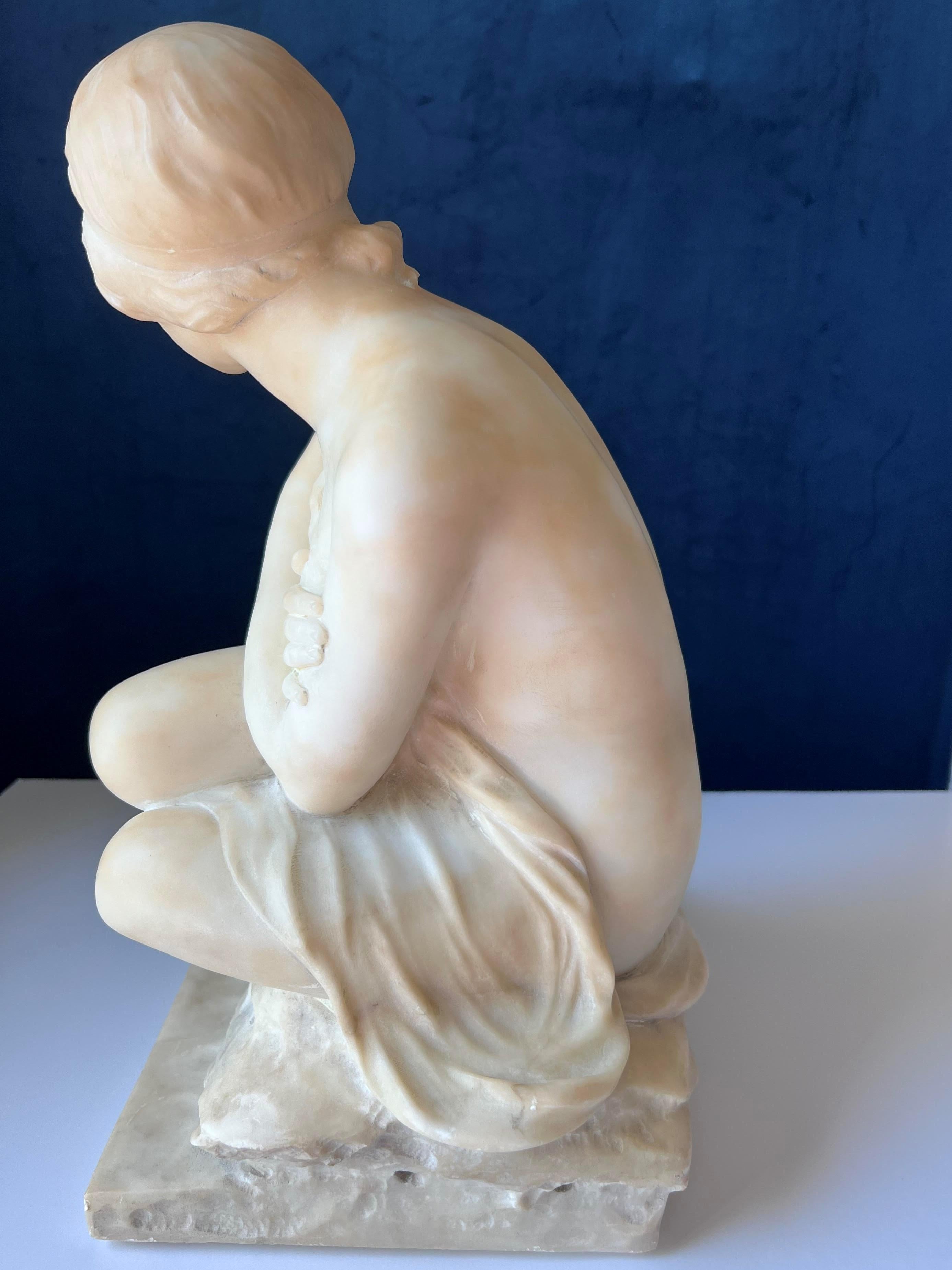 Anfang 20. Jh. Italienische Jugendstil-Alabaster-Skulptur einer jungen Badenden.  Der Badende sitzt mit verschränkten Armen in bescheidener Pose auf einem Stein.  Der Badende ist halbnackt.  Einige kleinere Schrammen und Kratzer.  Die Skulptur ist