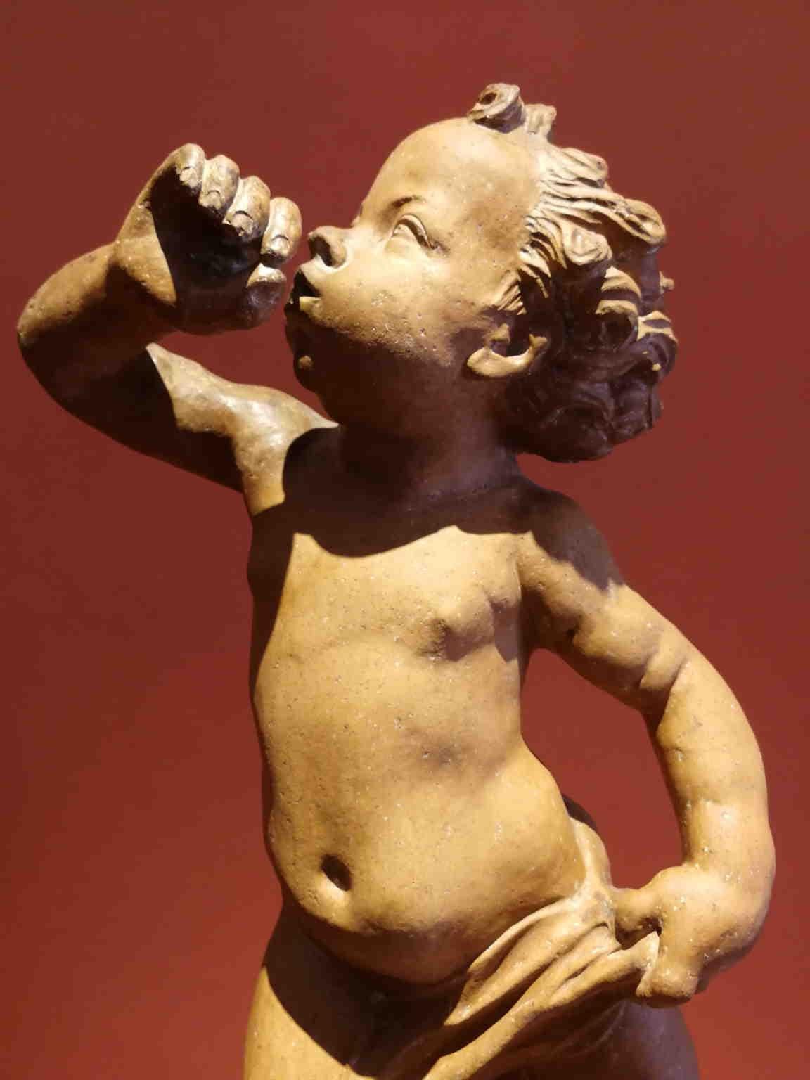 Terracotta statue representing a putto blowing with a cloth around his leg. It's inspired by the putto with dolphin by Andrea del Verrocchio, made for a fountain in Palazzo Vecchio (Florence). Considering the position, the typology of the objetc and