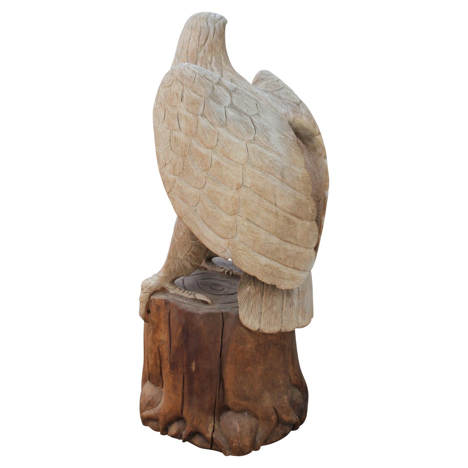 Hand carved statue of red-eyed eagle facing left and perched on a wooden log. The eagle's body has been brushed with white and the stump has been left a natural color. 