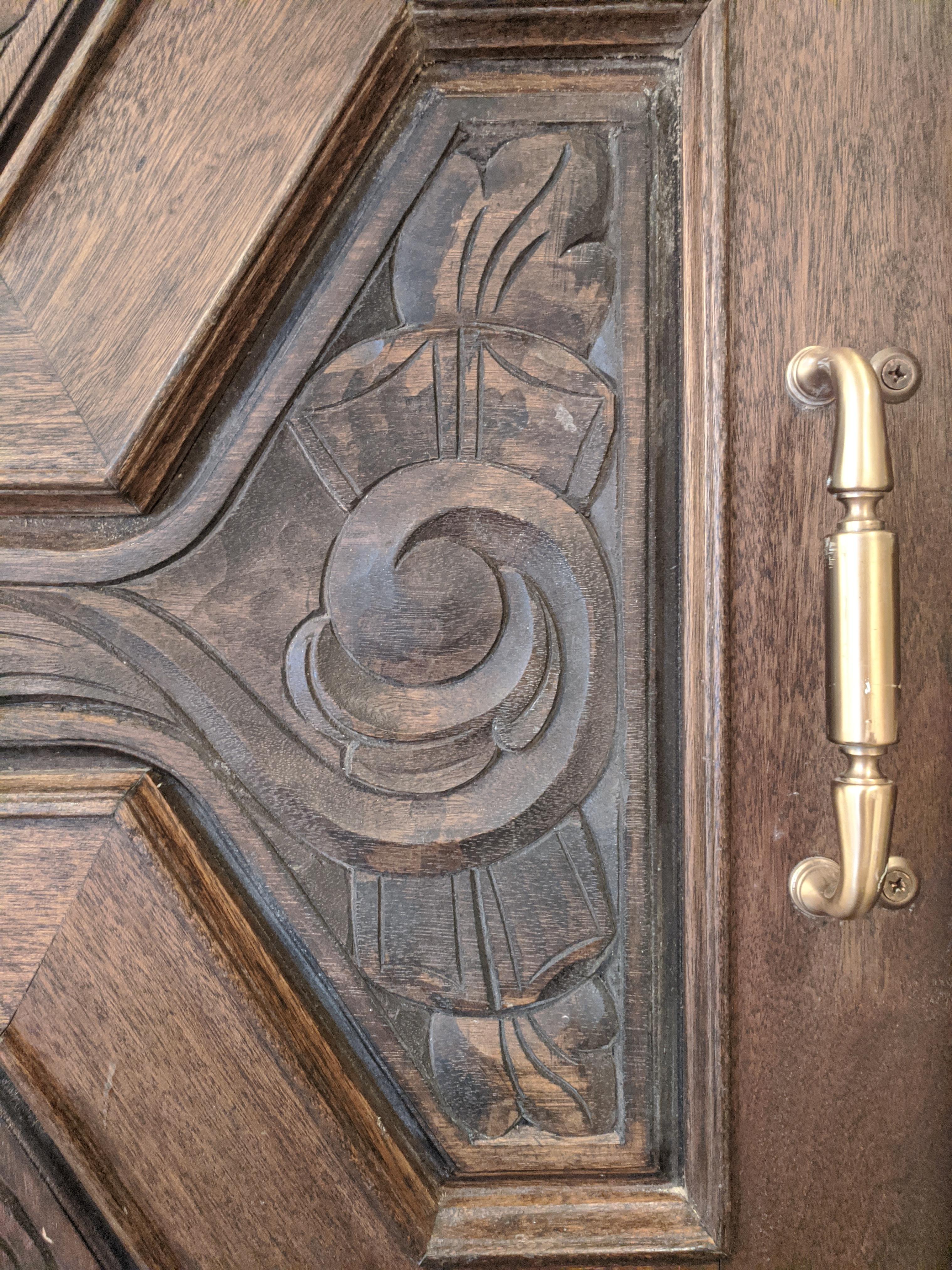 These massive wooden doors make a strong statement wherever they are placed. Hand carved with panels of an art-deco design, they are stained in a walnut color. The precise wood used is undetermined. Each door weighs between 60-70pounds. The doors