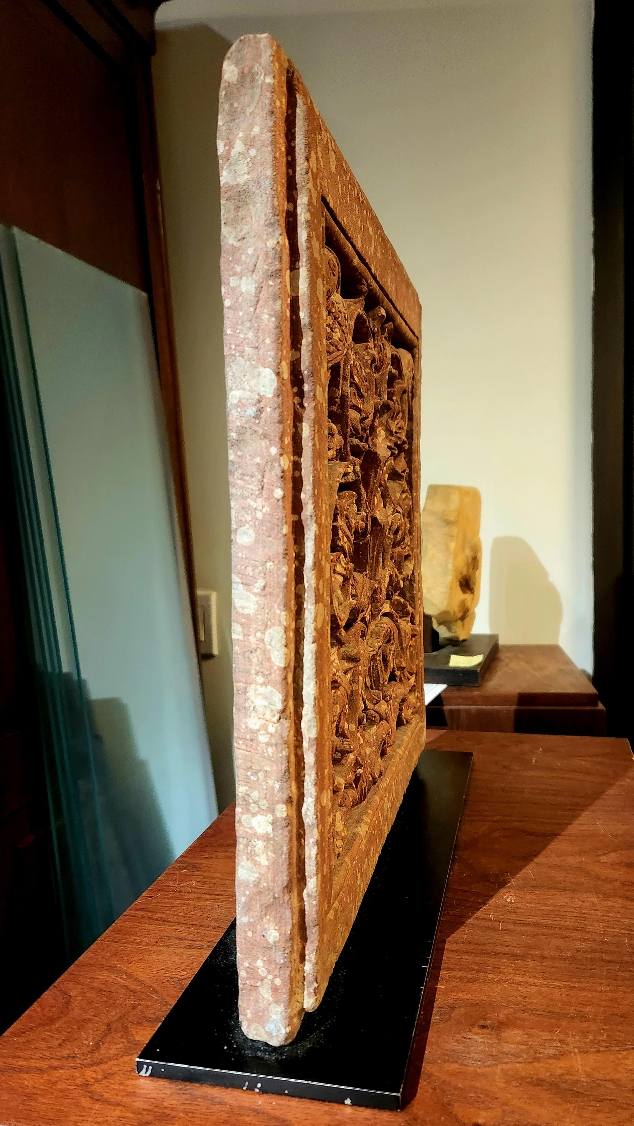 Indian relief panel from the 18th century in mottled red sandstone and in Mughal style from Rajastan. It is carved with an elaborate and stylized tree-of-life motif. From a fluted vase with a scalloped rim sprouts a vigorous taut central