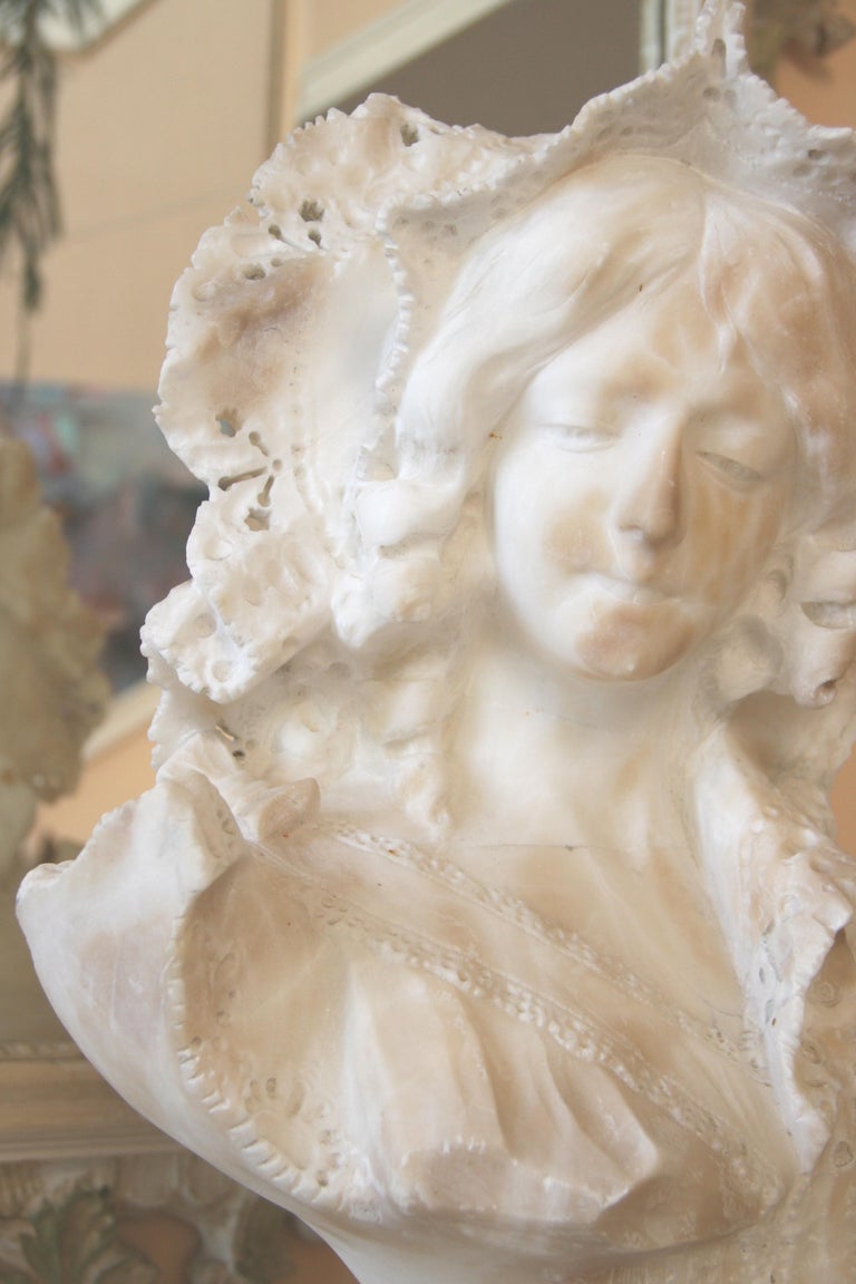 #9-440 Hand curved Art Nouveau alabaster bust of a young woman.Her elaborate hat framing a beautiful face .The style of clothing of the late 19th centuryArt Nouveau period.The bust rest on a round marble pedestal base.