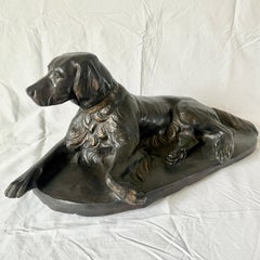 Large cast bronze sculpture of dog at rest, dark patina w/ gold-tone highlights.