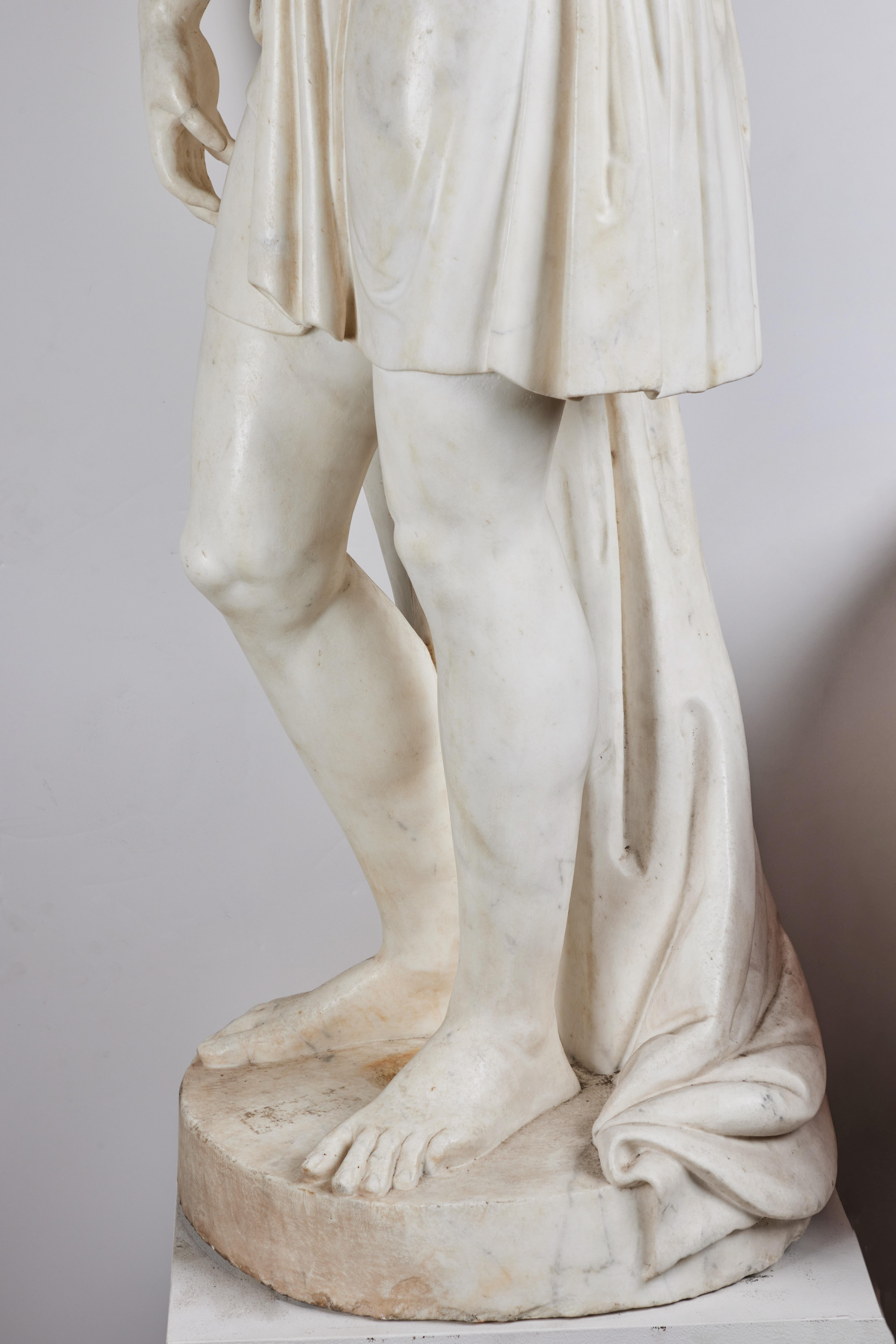 Eine wunderschön handgeschnitzte, lebensgroße Figur aus Carrara-Marmor, die einen Jungen darstellt. Das Gewand ist elegant mit Spangen drapiert.