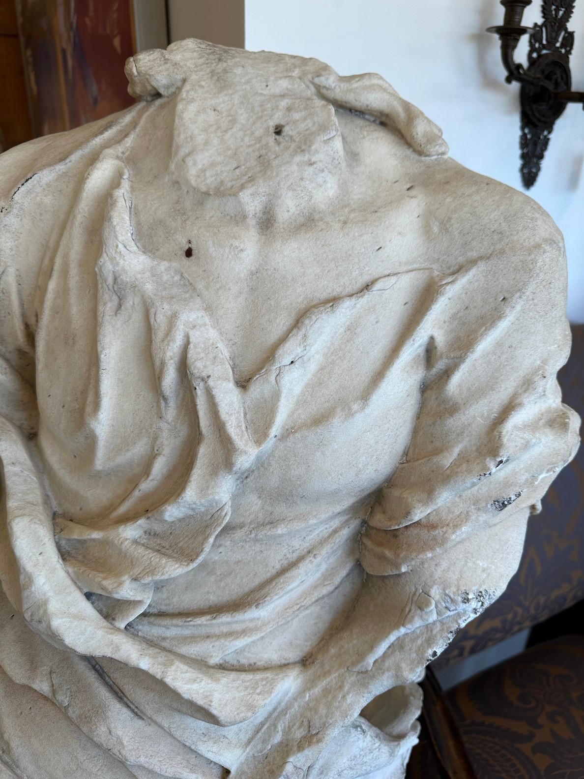 An extraordinary 17th century, hand-carved, solid Carrara marble, life sized figure fragment on raised base of the same. The subject is swaddled in a luxurious, gathered robe and tunic and features the remains of long, cascading tendrils of hair.