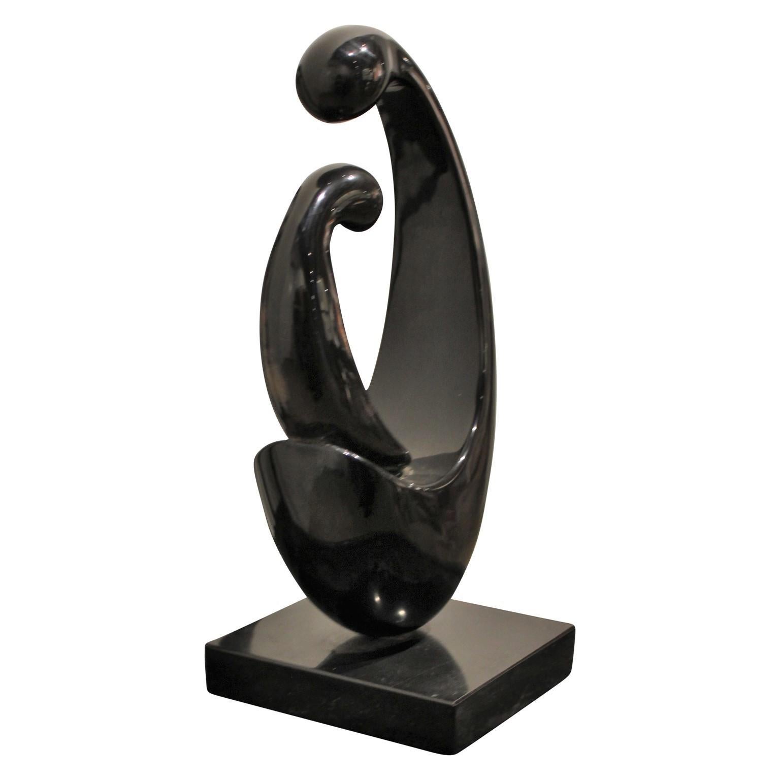 Black marble figurative sculpture of two figures. One appears to be a smaller figure sitting in the lap of the larger one. Sculpture sits on a matching pedestal. 