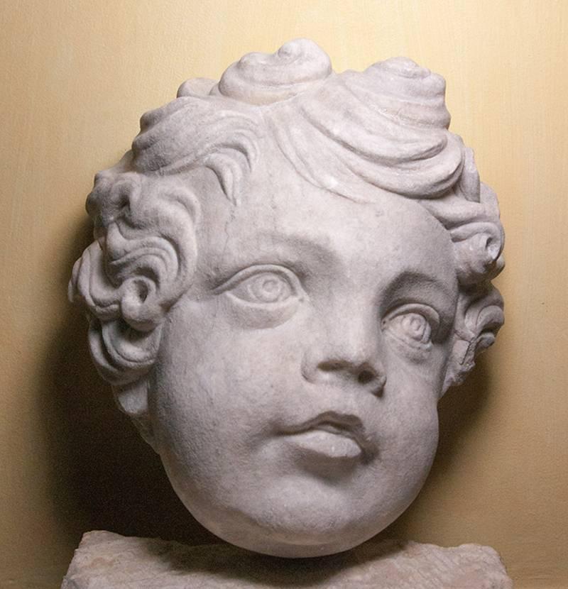 A larger than life marble head of a putto or child, most probably from an altar decoration. The putto show animation and movement, especially in the carving of the cheeks and lips. The head is turned to the left.
This treatment creates a contrast of