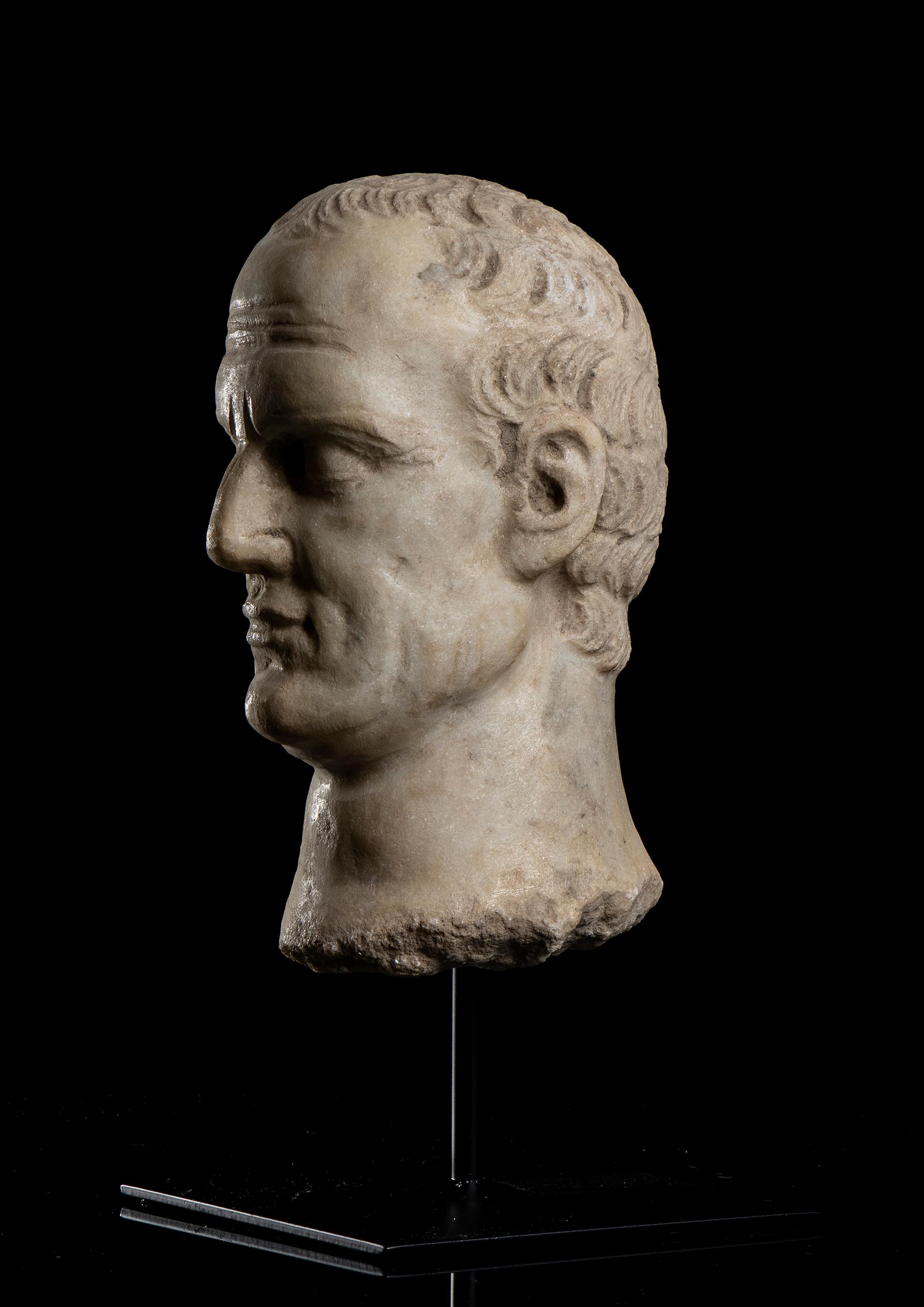 Der Kopf von Jiulis Caesar steht auf einem zentralen Stift auf einem quadratischen Sockel aus schwarzem Metall in einem archäologischen Grand Tour Stil, klassisch römisch geschnitzt in weißem statuarischem Marmor gealtert.
Gaius Julius Cäsar  war