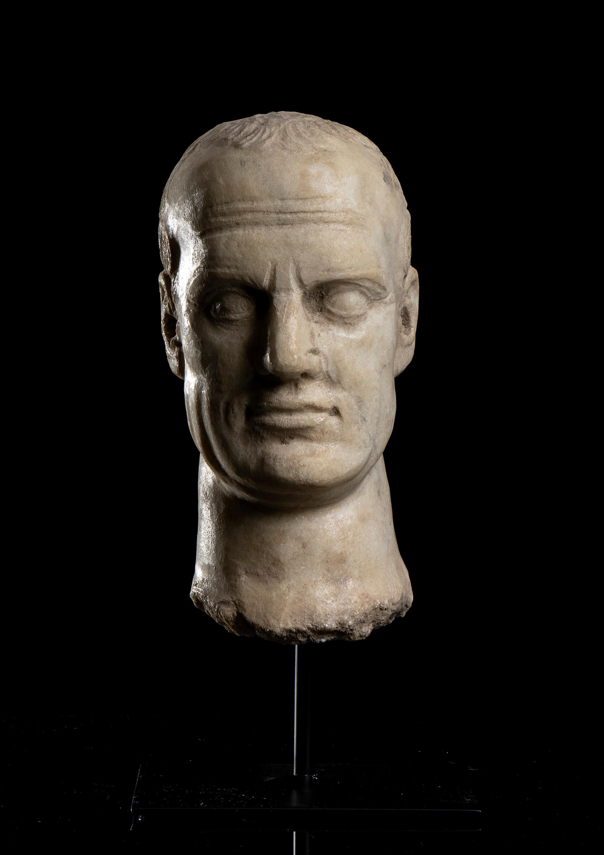 The head of Jiulis Caesar stand on a central pin on a squared base in black metal in an archeological grand tour style, classical Roman carved in white statuary marble aged.
Gaius Julius Caesar  was the most important and influent  Roman general and