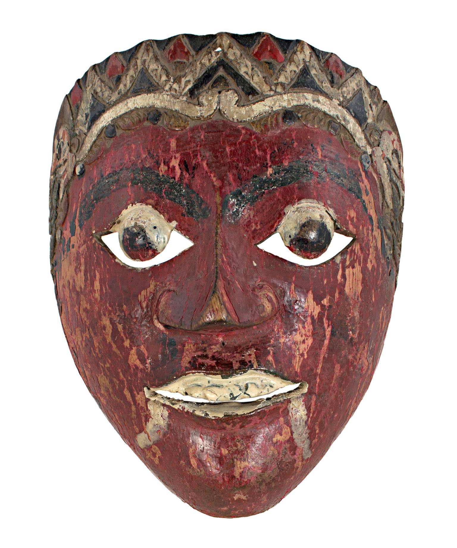 Ce masque, créé par un artiste indonésien inconnu, présente des yeux ronds, des crocs peints et un visage rouge sang. Il mesure environ 7 1/4