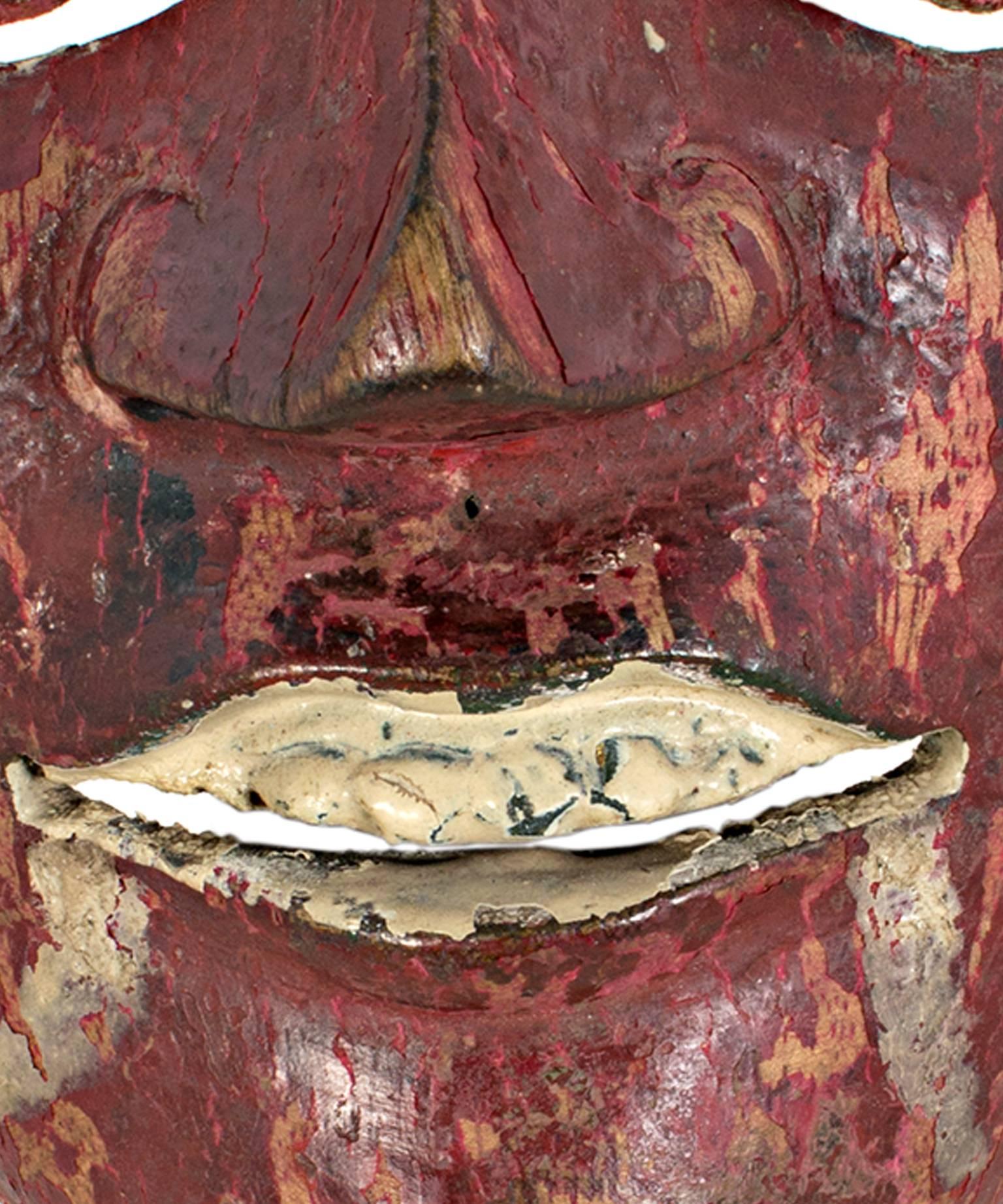 This mask, created by an unknown Indonesian artist, features round eyes, painted fangs, and a blood red face. It is approximately 7 1/4
