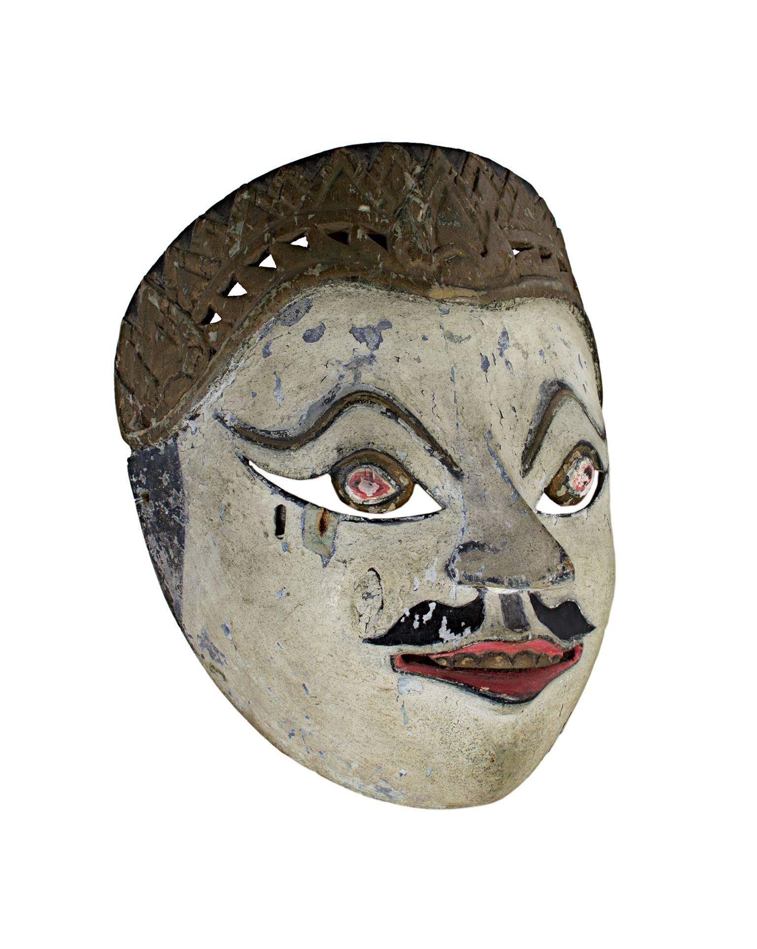 Ce masque, créé par un artiste indonésien inconnu, présente des yeux ronds, un visage blanc et une moustache peinte. Il mesure environ 7 pouces de haut et 5 1/2 pouces de large. 