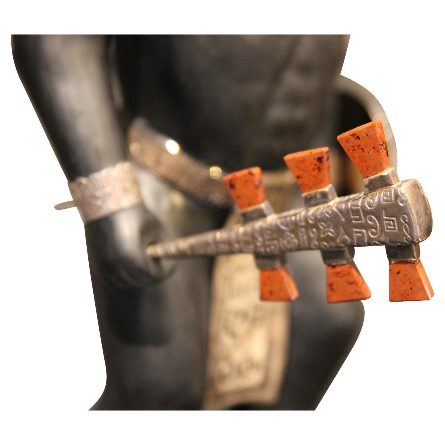 Mayan or Aztec warrior sculpture with lapis, malachite, and tiger's eye inlay. The sculpture's club is a detachable metal piece with an orange-colored precious stone. The sculpture sits on a base with a decorative metal rim. 