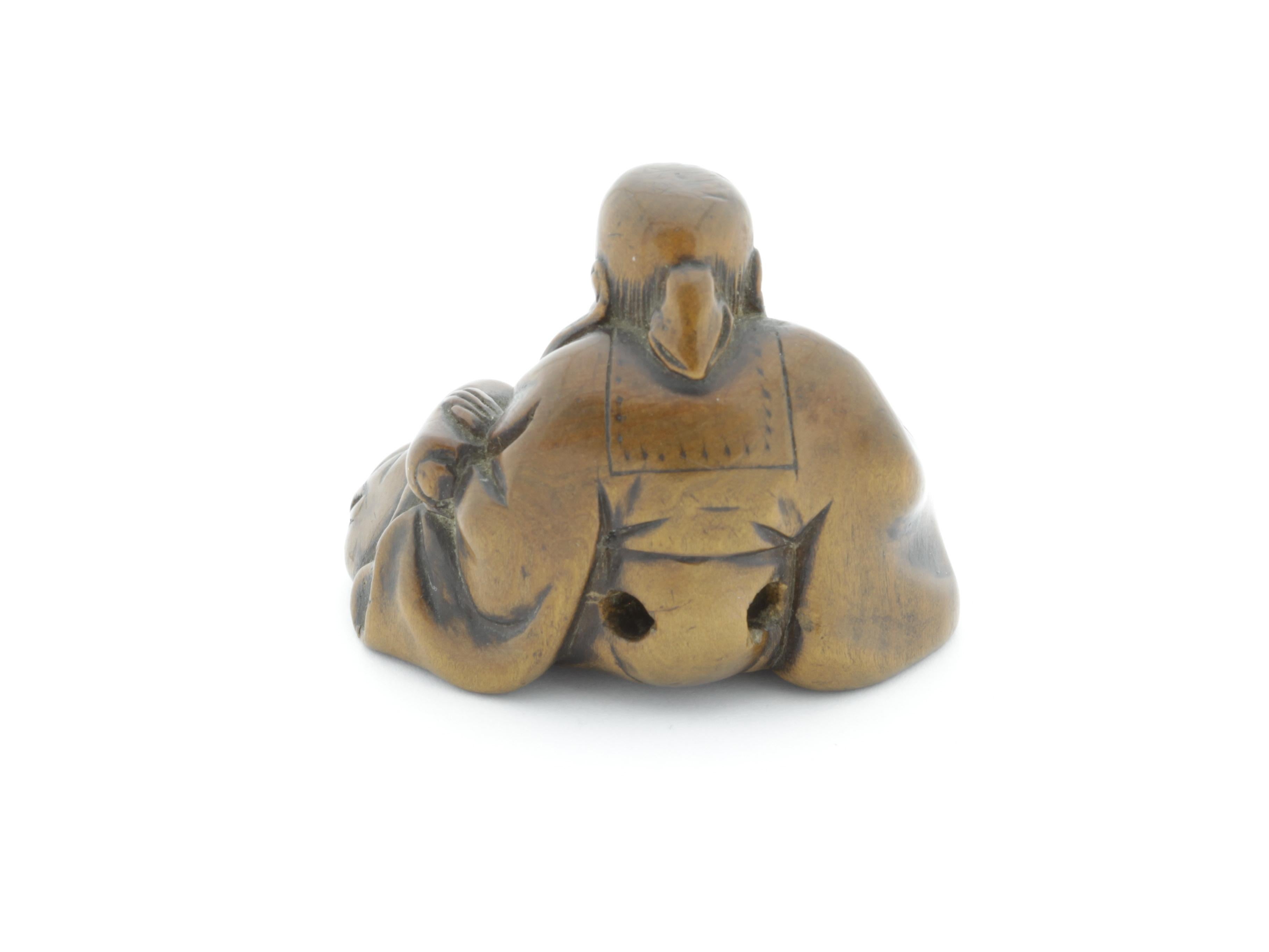 This netsuke is made entirely out of wood and shows one of the Seven Gods of Fortune, Fukurokuju. He is the deity of wisdom, good luck, happiness, wealth, virility and longevity. In here, he is holding a scroll with his left hand and is looking at a