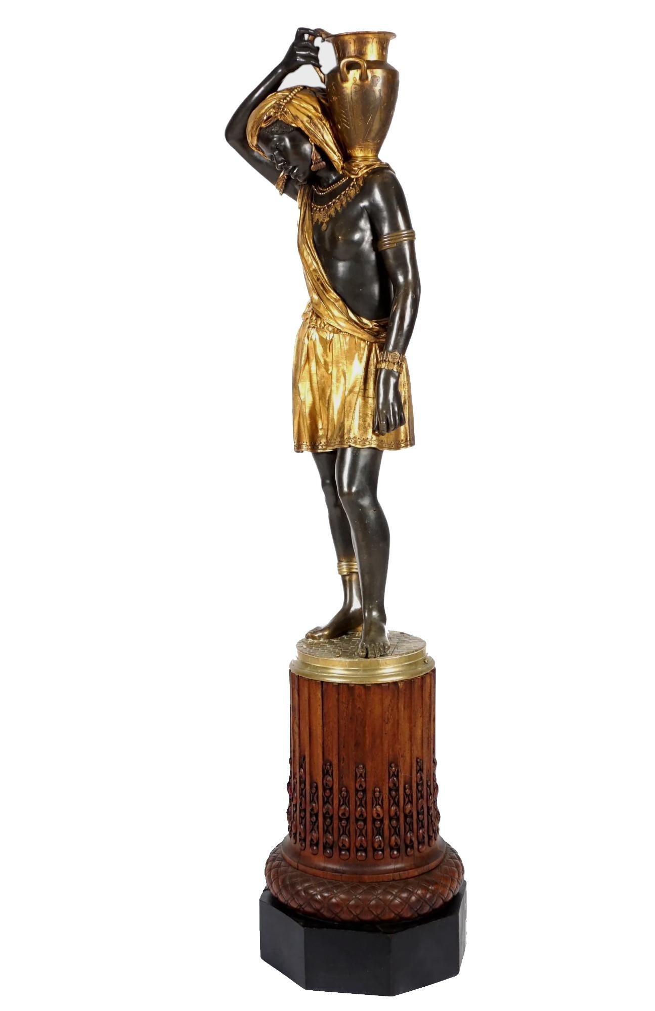 Parcel gilt and patinated bronze figural statue of a Nubian Water carrier with a pitcher on her shoulder. The contrast between the deep bronze and bright gilding is incredibly striking. The woman drips in gold jewelry and drapery, wearing arm