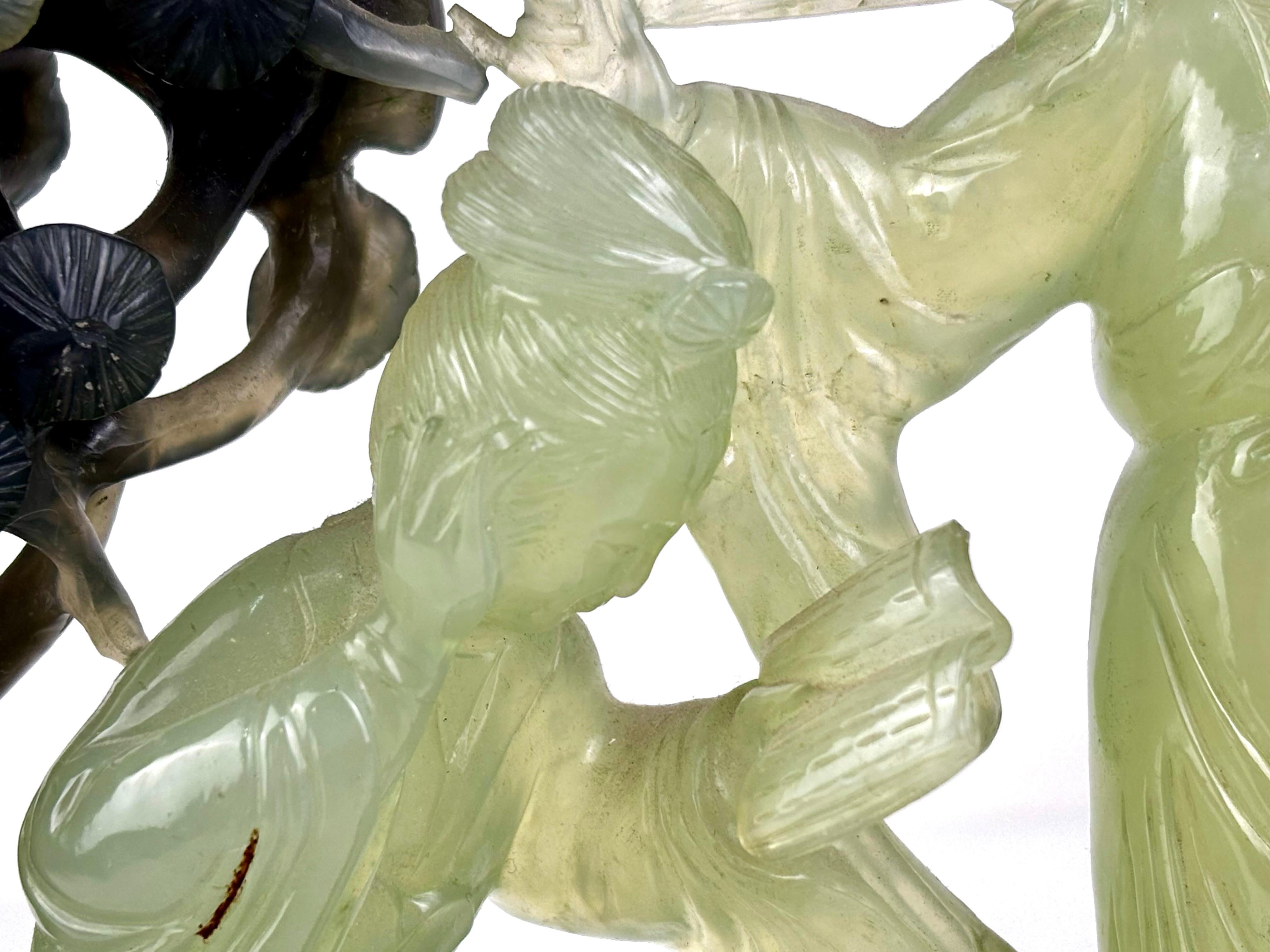 Elegant hand-carved bicolor jade sculpture from the Oriental tradition, depicting two court ladies beneath a flowering tree. The figures are crafted in translucent light green jade, while the tree is carved in a darker tone, creating a refined