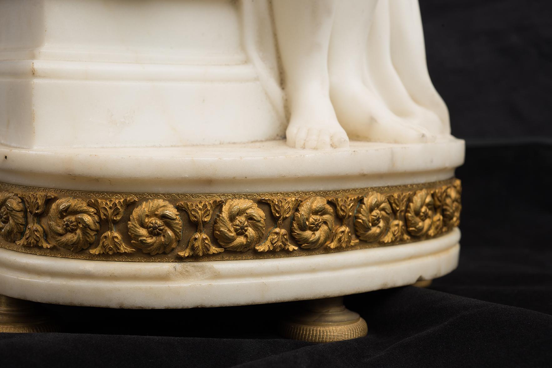 Antique white marble statuary clock belonging to the Napoleon III period of the second half of the 19th century.

A woman holding a book rests on a column with a porcelain dial in the center.

The base wrapped in a gilded bronze garniture rests on