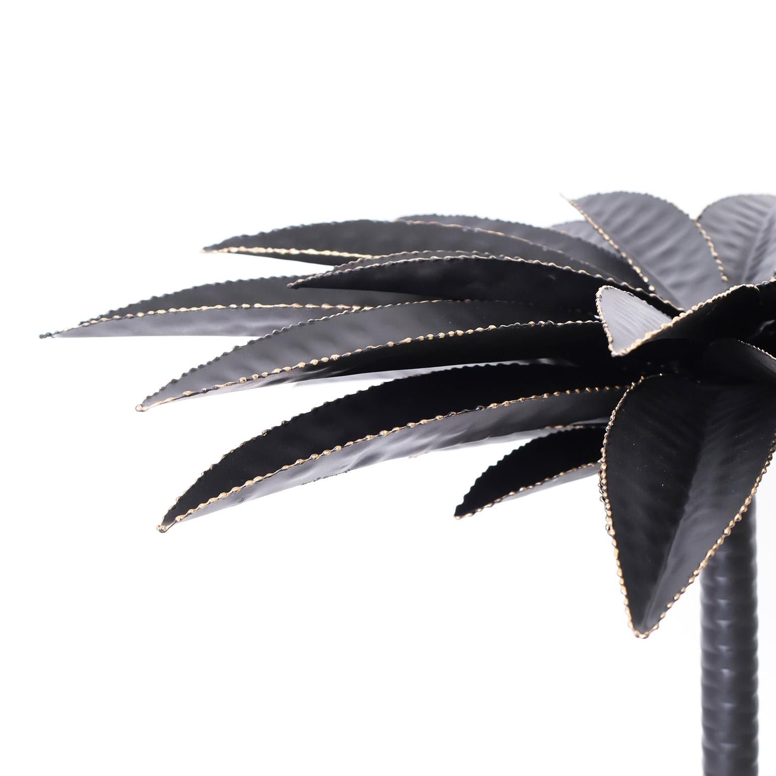 Pair of tole or painted metal potted palm trees with stylized palm leaves having serrated edges on a trunk in a geometric planter with affixed black rocks.